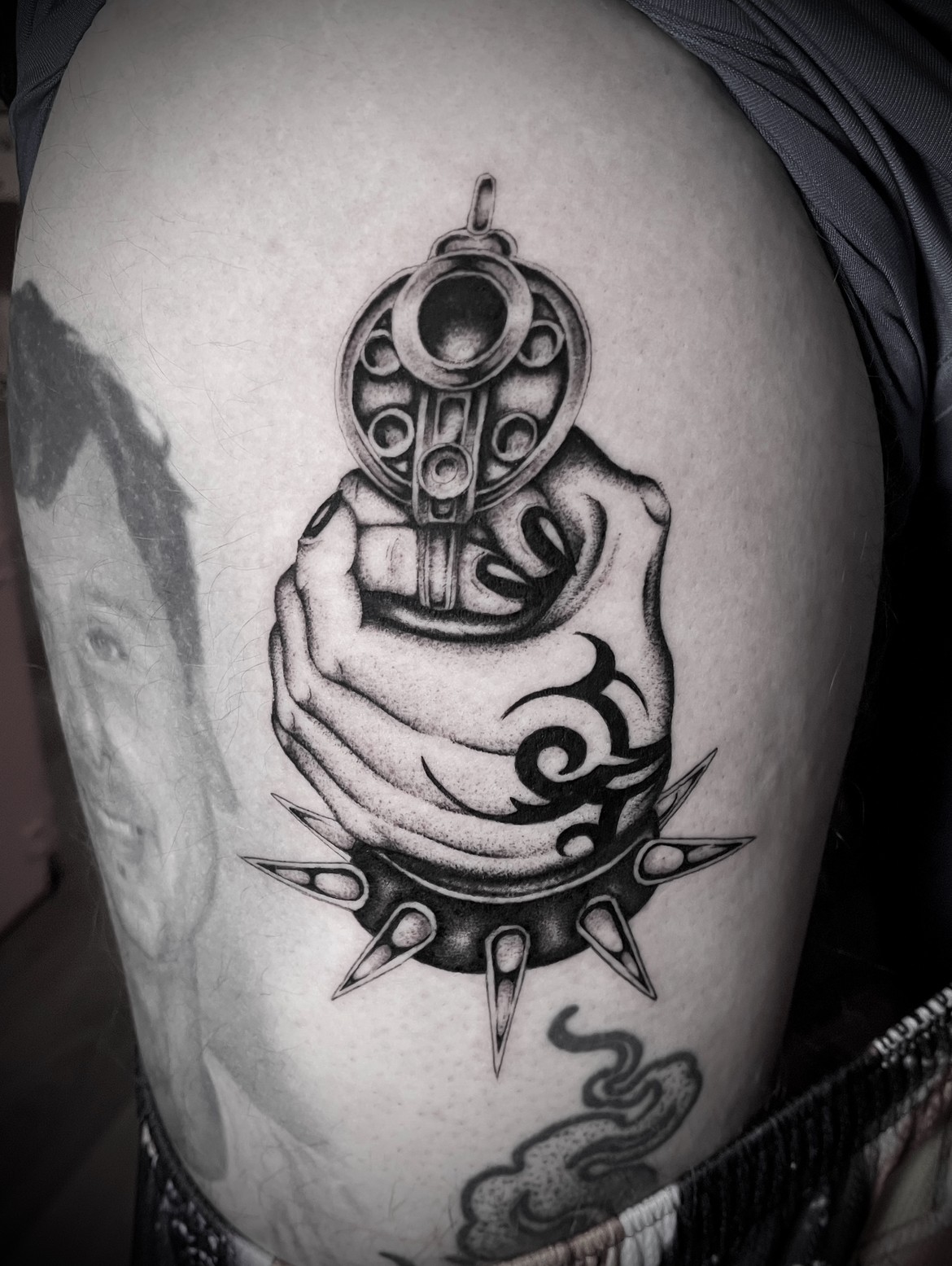 Tattoo of a hand holding a revolver with intricate design, surrounded by a circular pattern and a stylized cloud below.