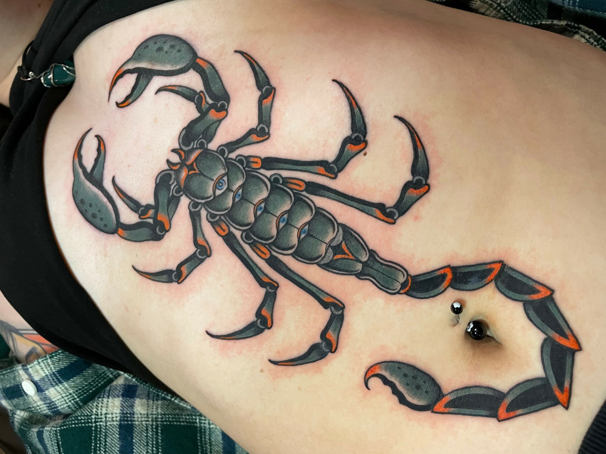 Scorpion tattoo on person's side with a piercing near the tail, detailed black and orange coloring, and a realistic style.