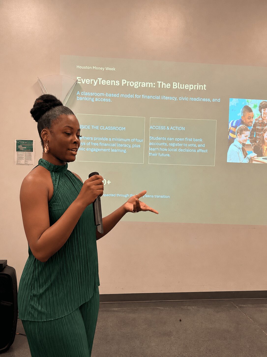 Woman in green dress giving a presentation in front of a projected slide about a program called The Blueprint.