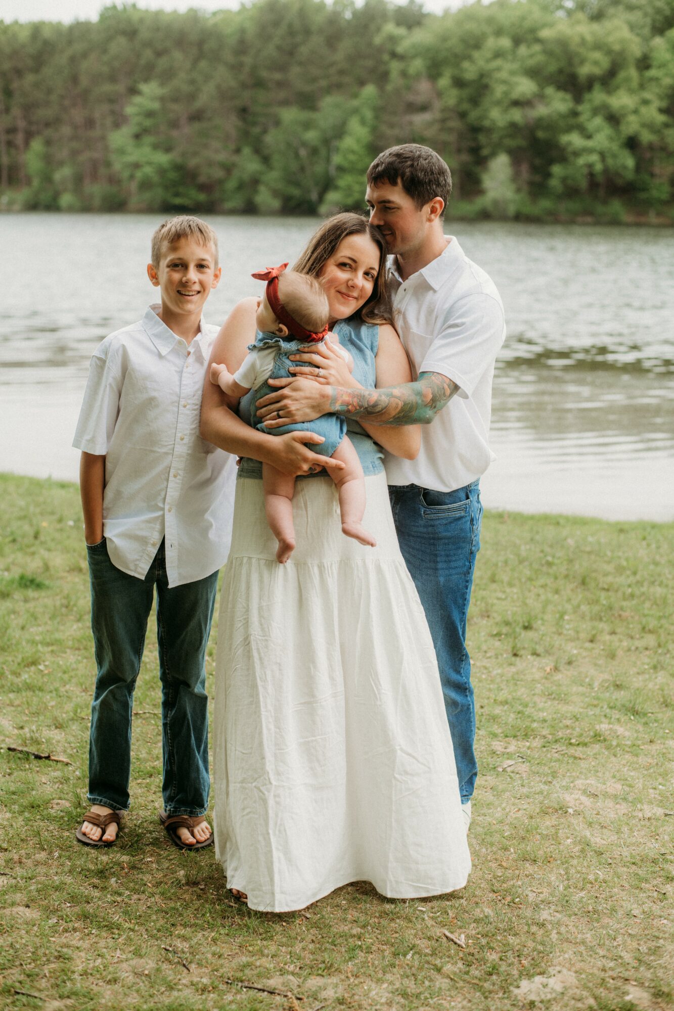 Family of four standing outdoors near a lake, smiling, with trees in the background.