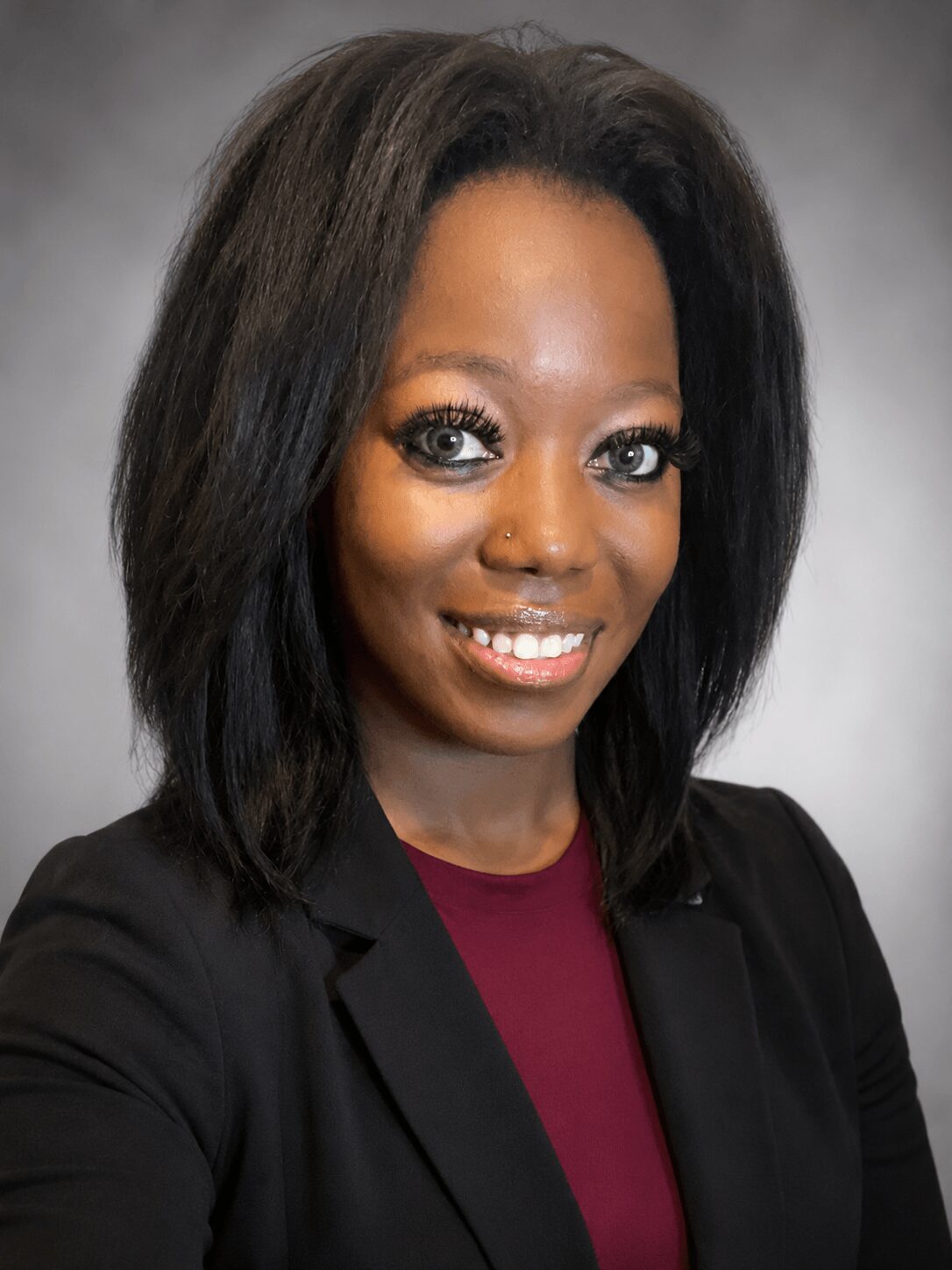 Portrait of a woman with shoulder-length black hair, wearing a black blazer and maroon top, smiling.