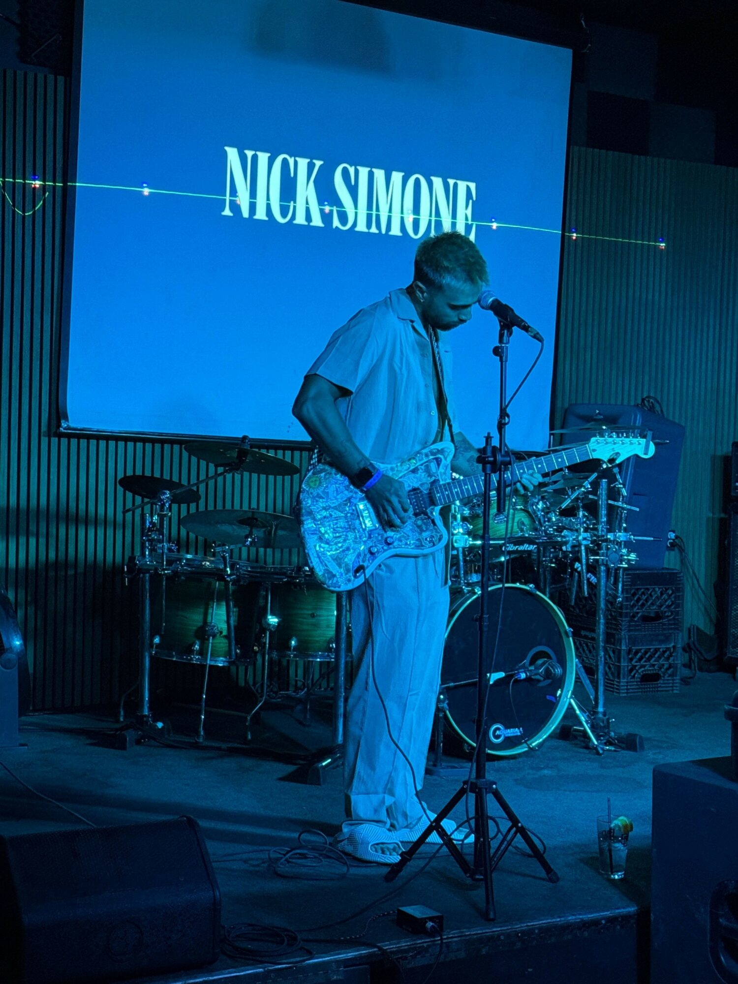 Person in white clothing performing science experiment with glassware and equipment on table, large screen with text in background.