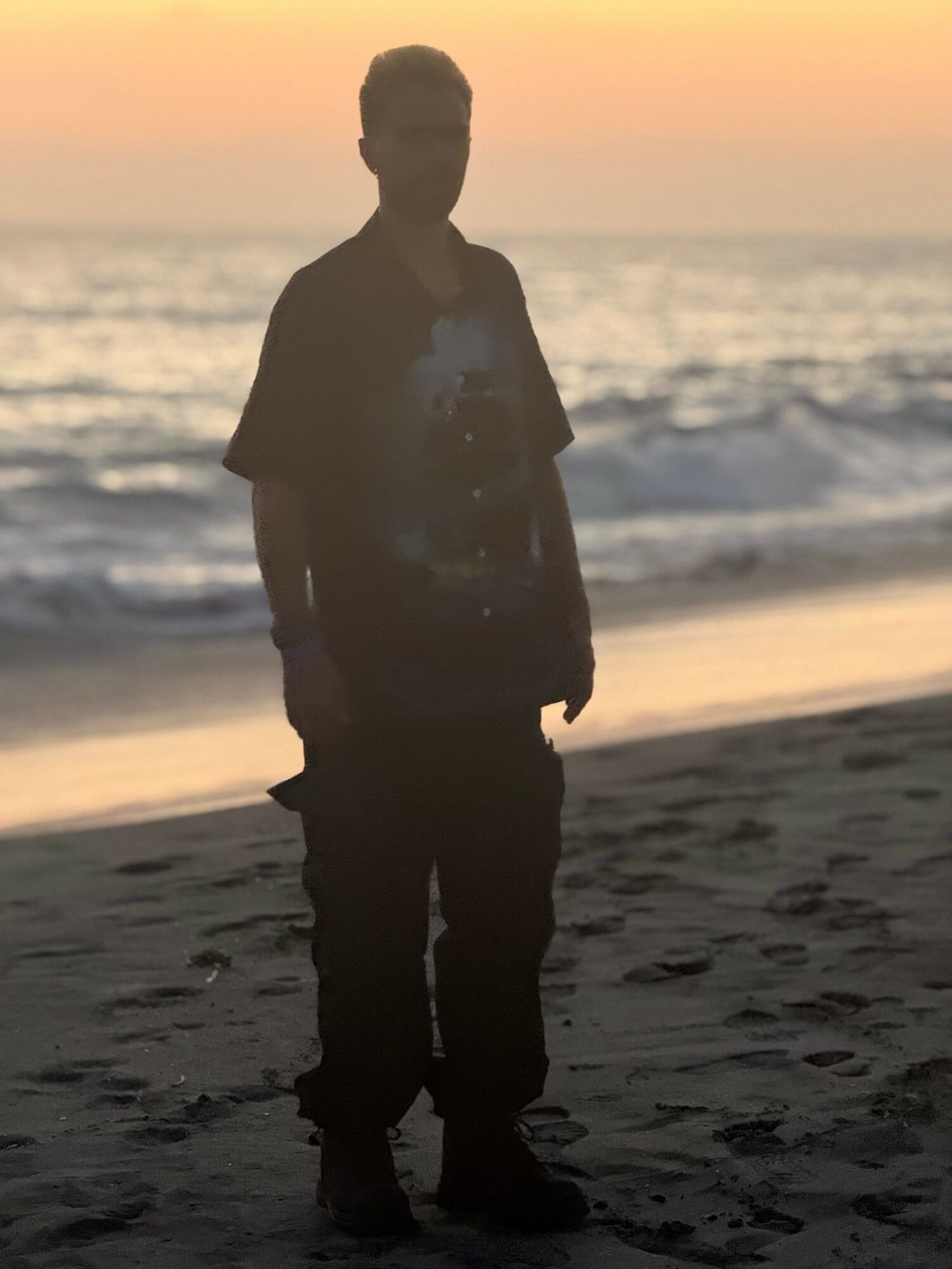 Silhouette of a person standing on a beach at sunset with the ocean in the background.