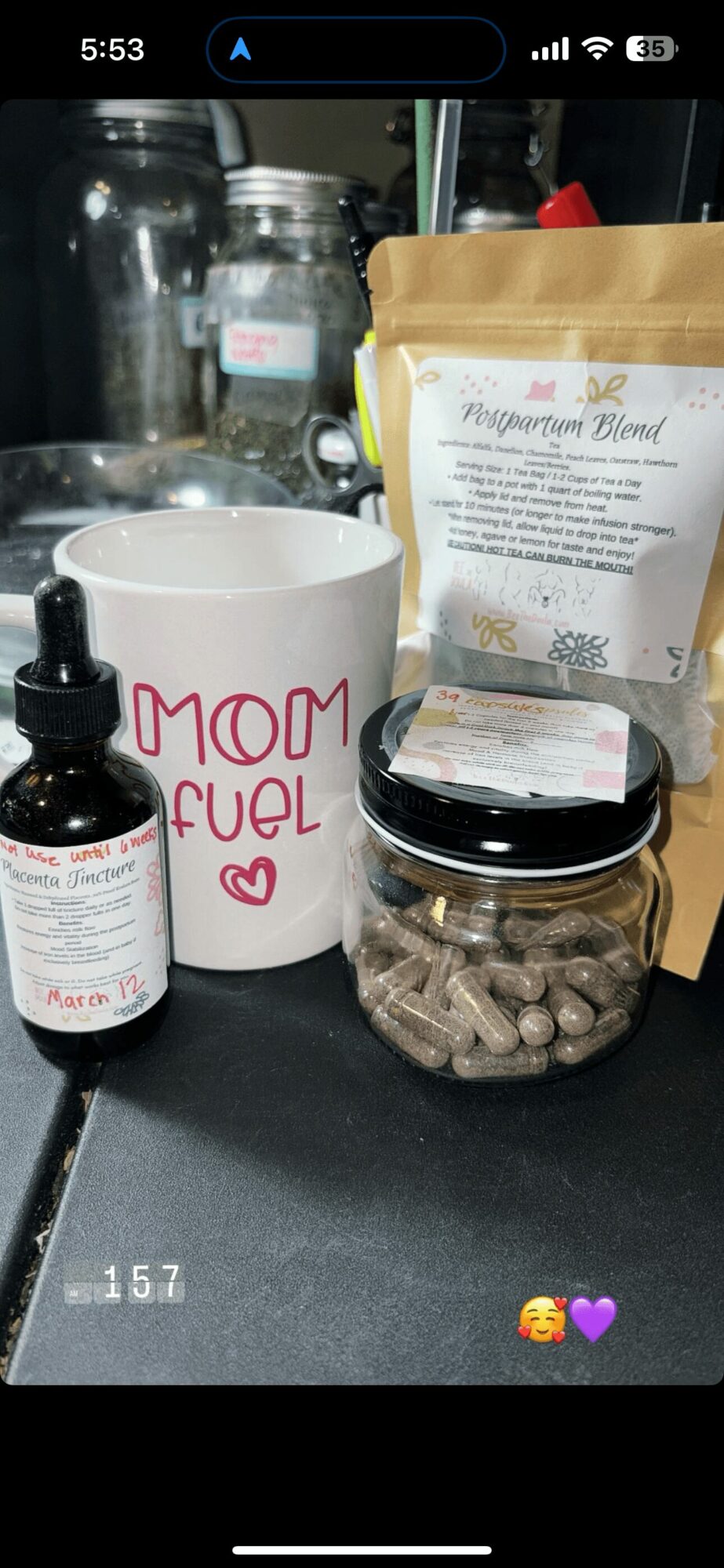 Coffee mug with 'MOM FUEL' text, jar of capsules, bottle, and a bag of ingredients on a black surface.