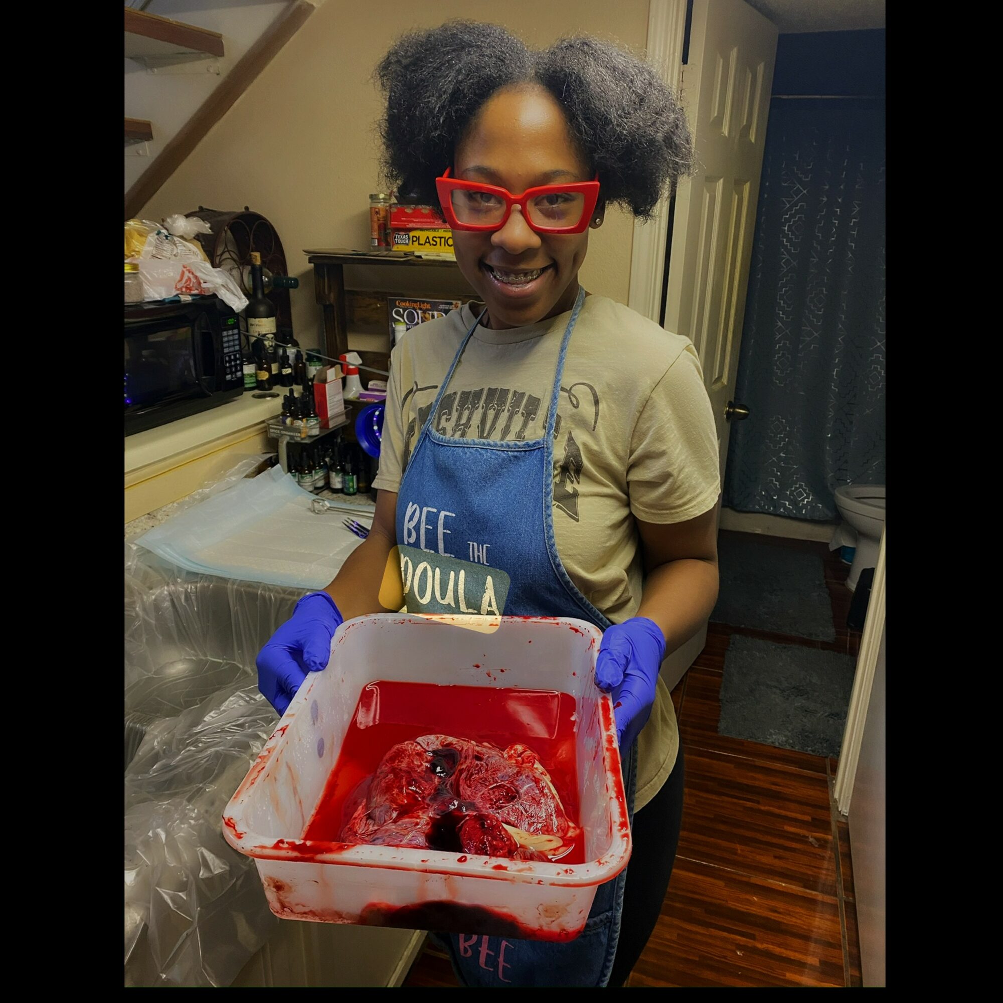 Child with glasses and apron holding a red container with raw meat, in a kitchen. Word on apron: 'DADDY'.