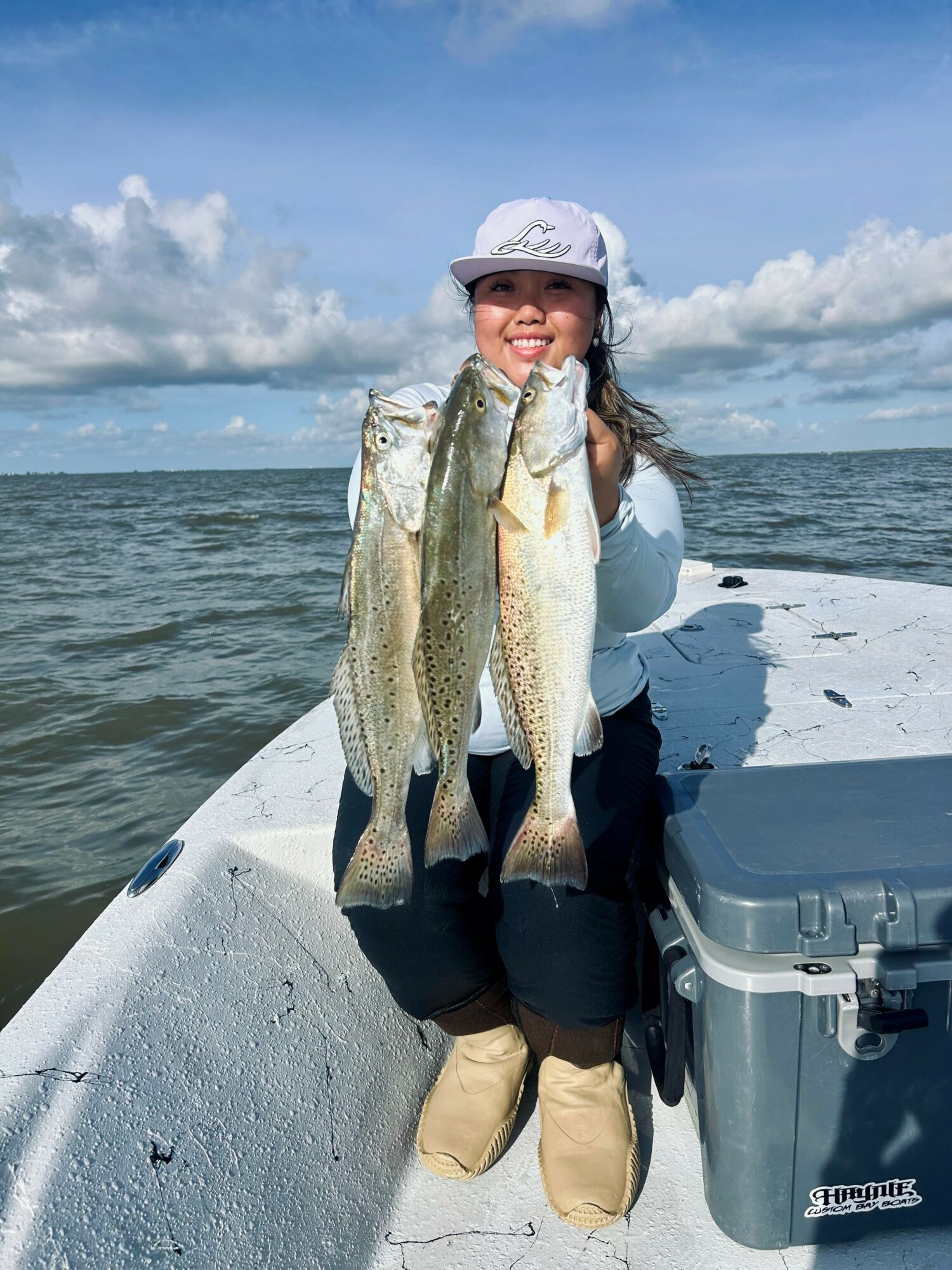 Smiling woman holding two large fish on a boat with water and sky in background.