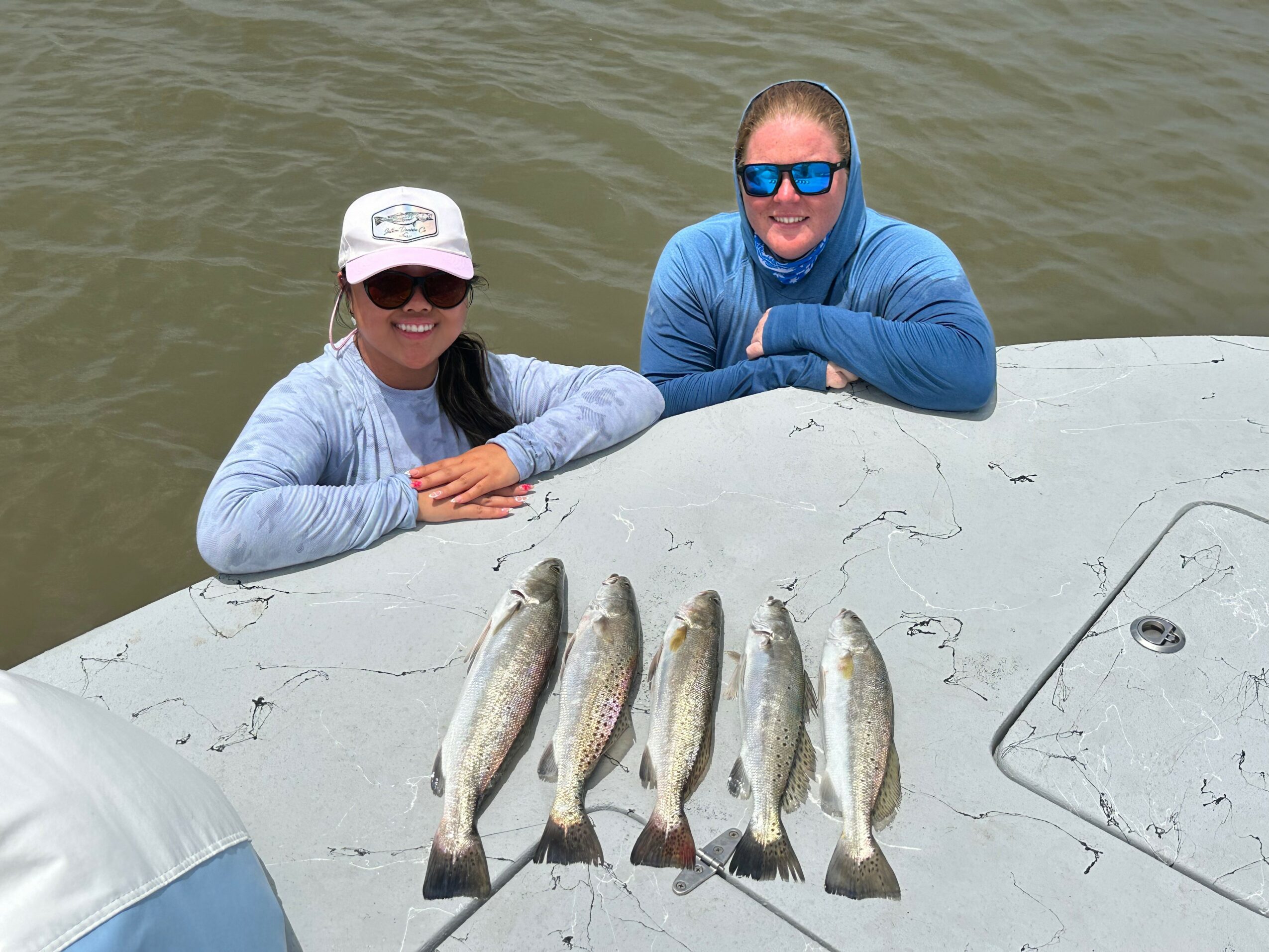 Two people smiling on a boat with five fish laid out in front, water in the background.