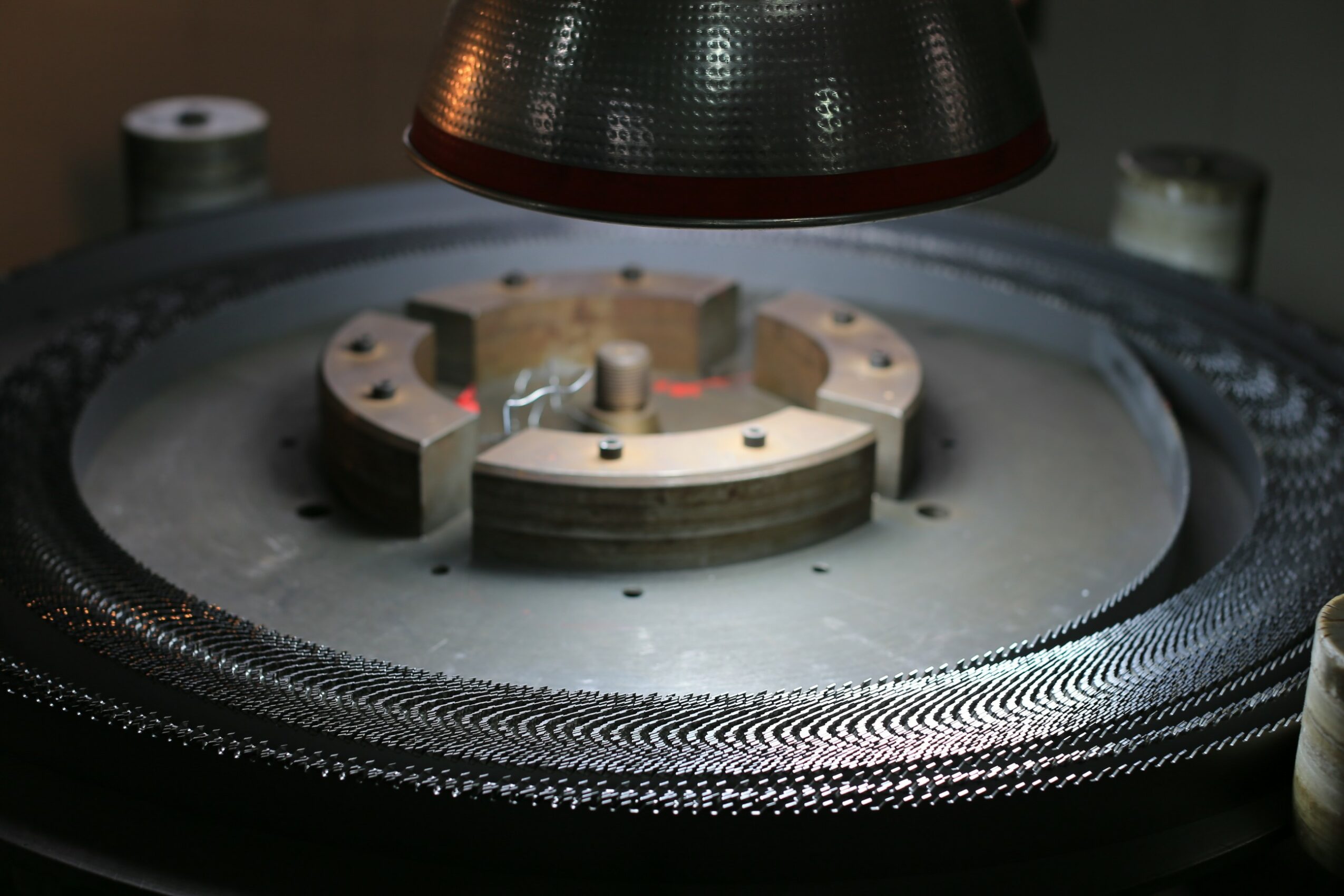 Close-up of a turntable with a metallic tonearm and a record, under a red-tinted light, with a blurred background.