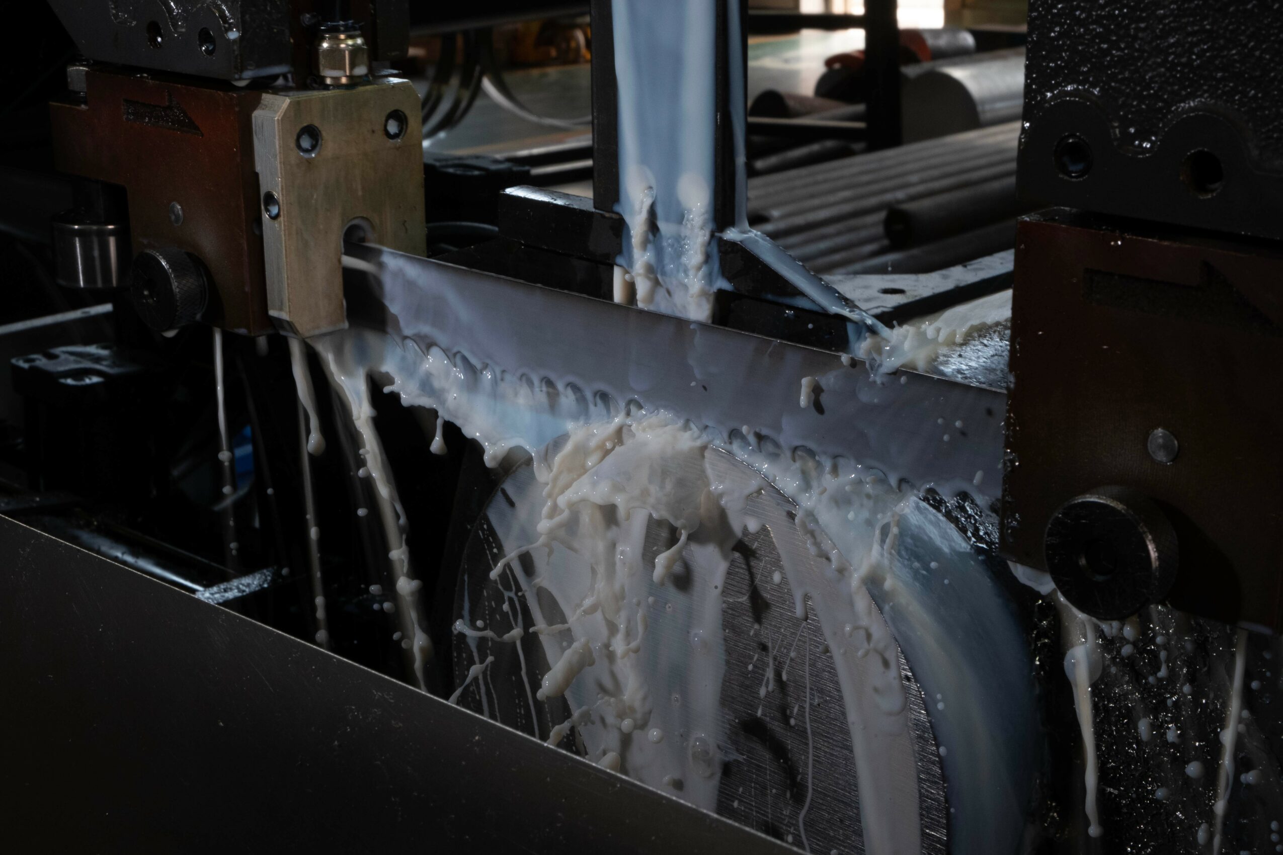 A saw blade cutting through a material with water spray cooling the blade, in a machine shop setting.