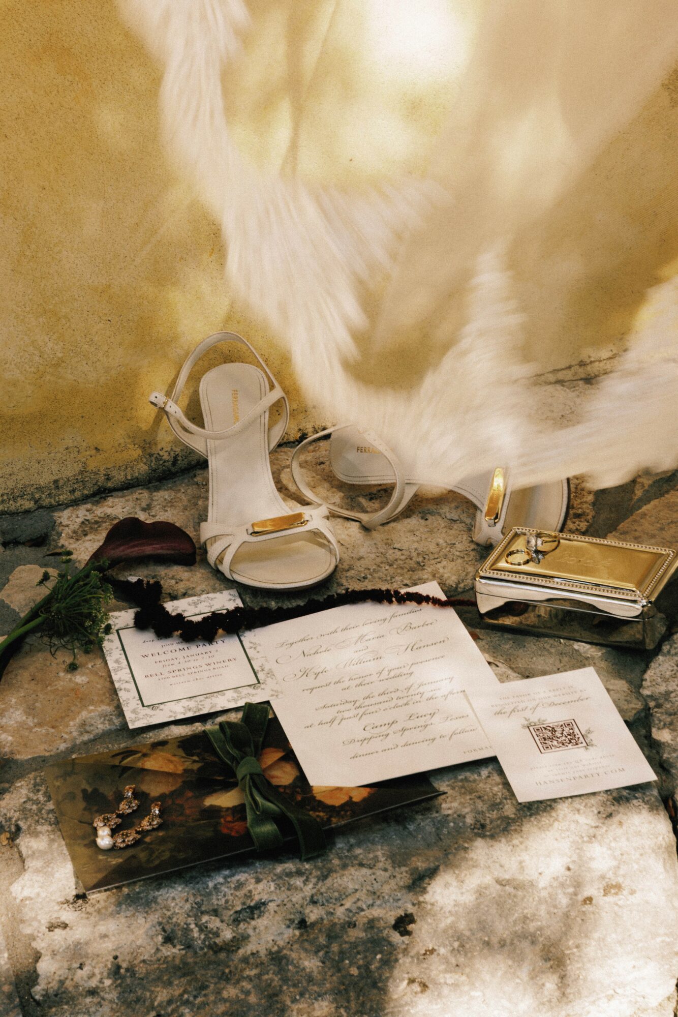 White cat sniffing papers and objects on a table, with a sandal and a small box nearby.