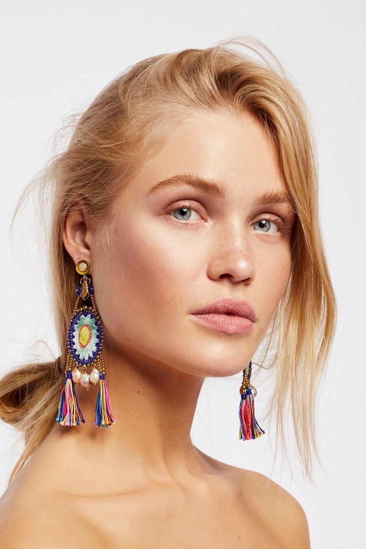 Close-up of a woman with blonde hair and blue eyes, wearing colorful earrings, looking at the camera.