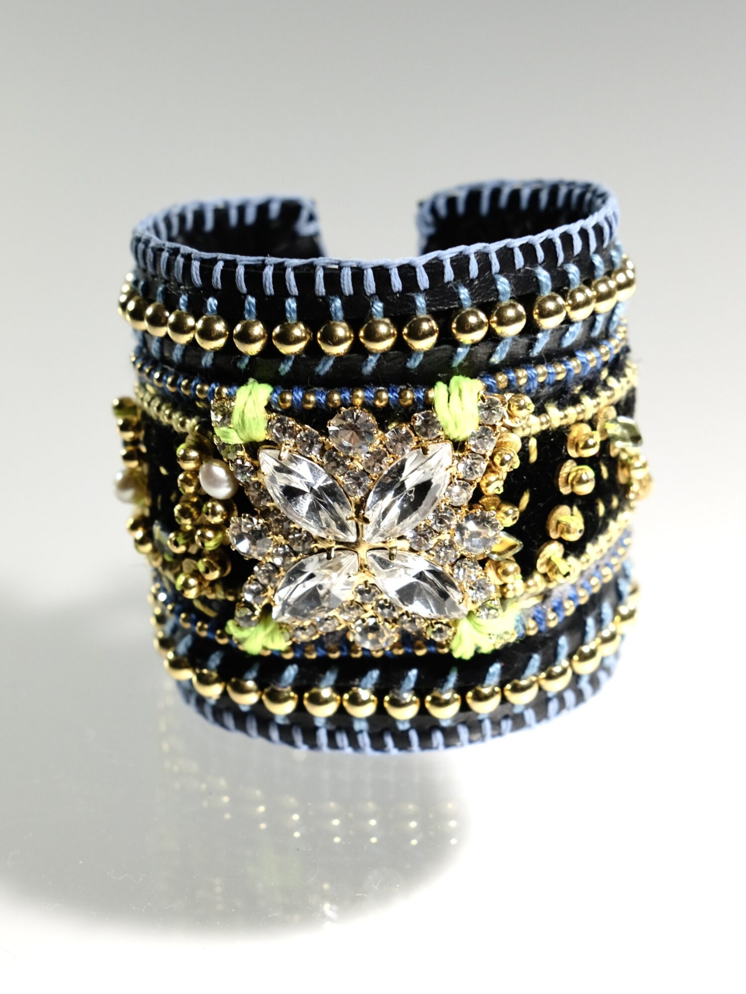 Wide bracelet with black, gold, and blue beads, featuring a large butterfly-shaped crystal centerpiece, on a reflective surface.