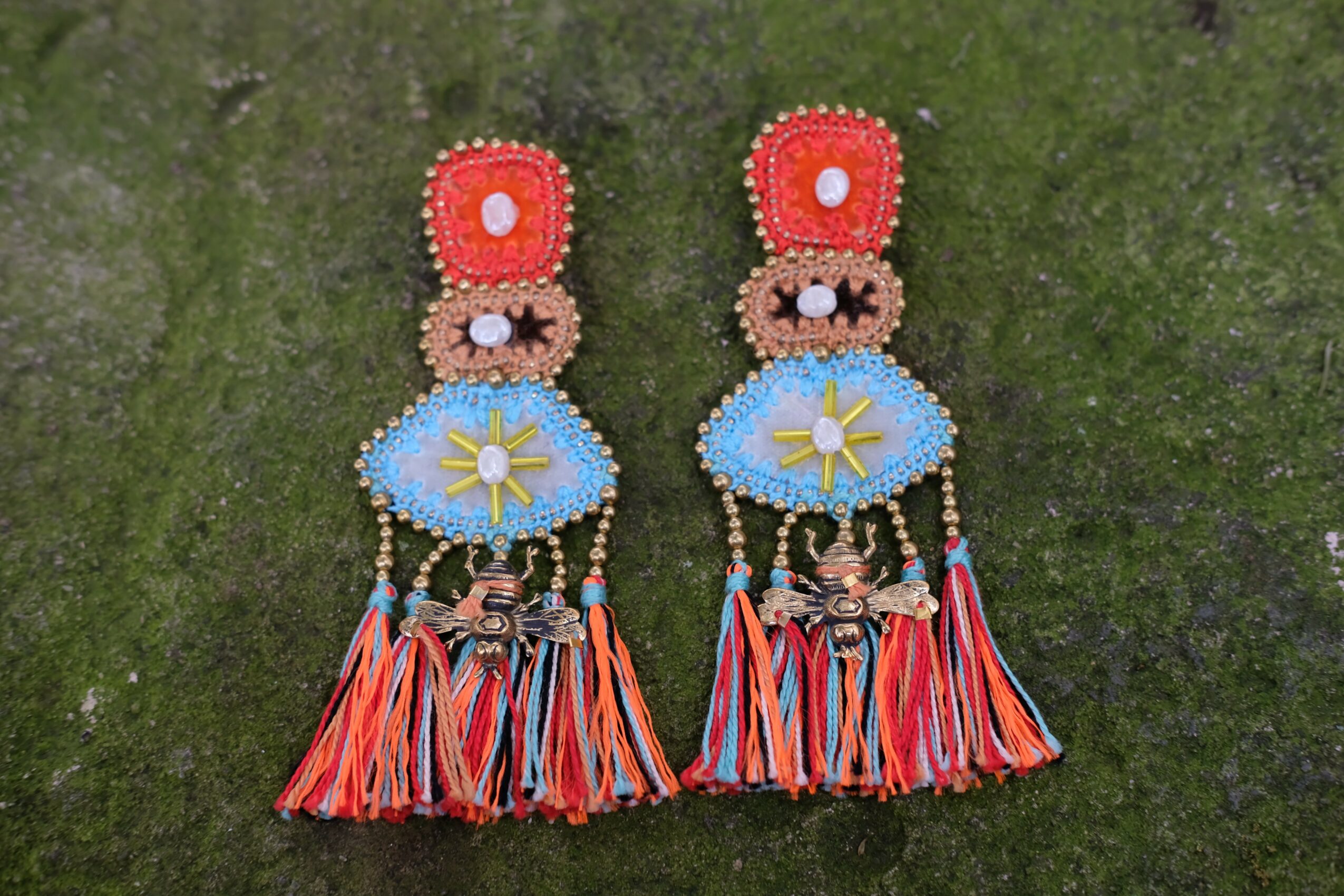 Pair of colorful beaded earrings with tassels, set against a mossy green background.