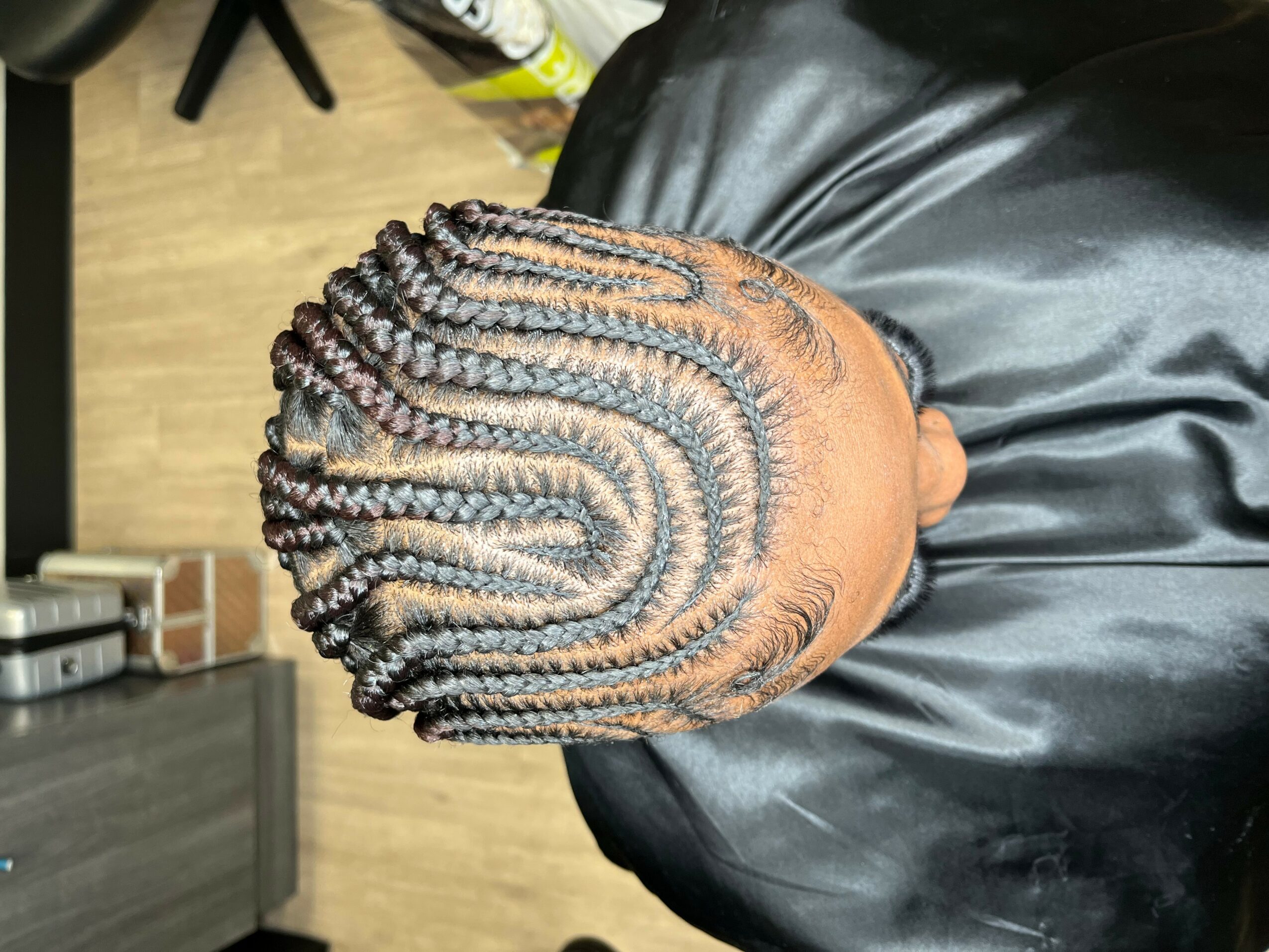 Top view of a person's head with braided hairstyle, showing intricate cornrows and extensions, on a black surface.