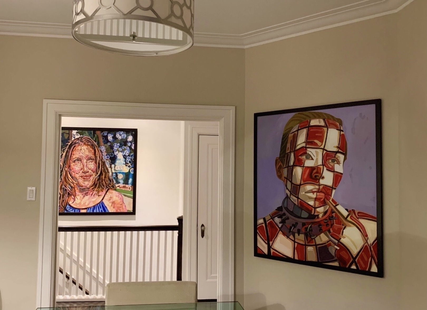 Two framed artworks on a beige wall, one of a woman and one of a geometric-patterned face, in a room with a doorway.