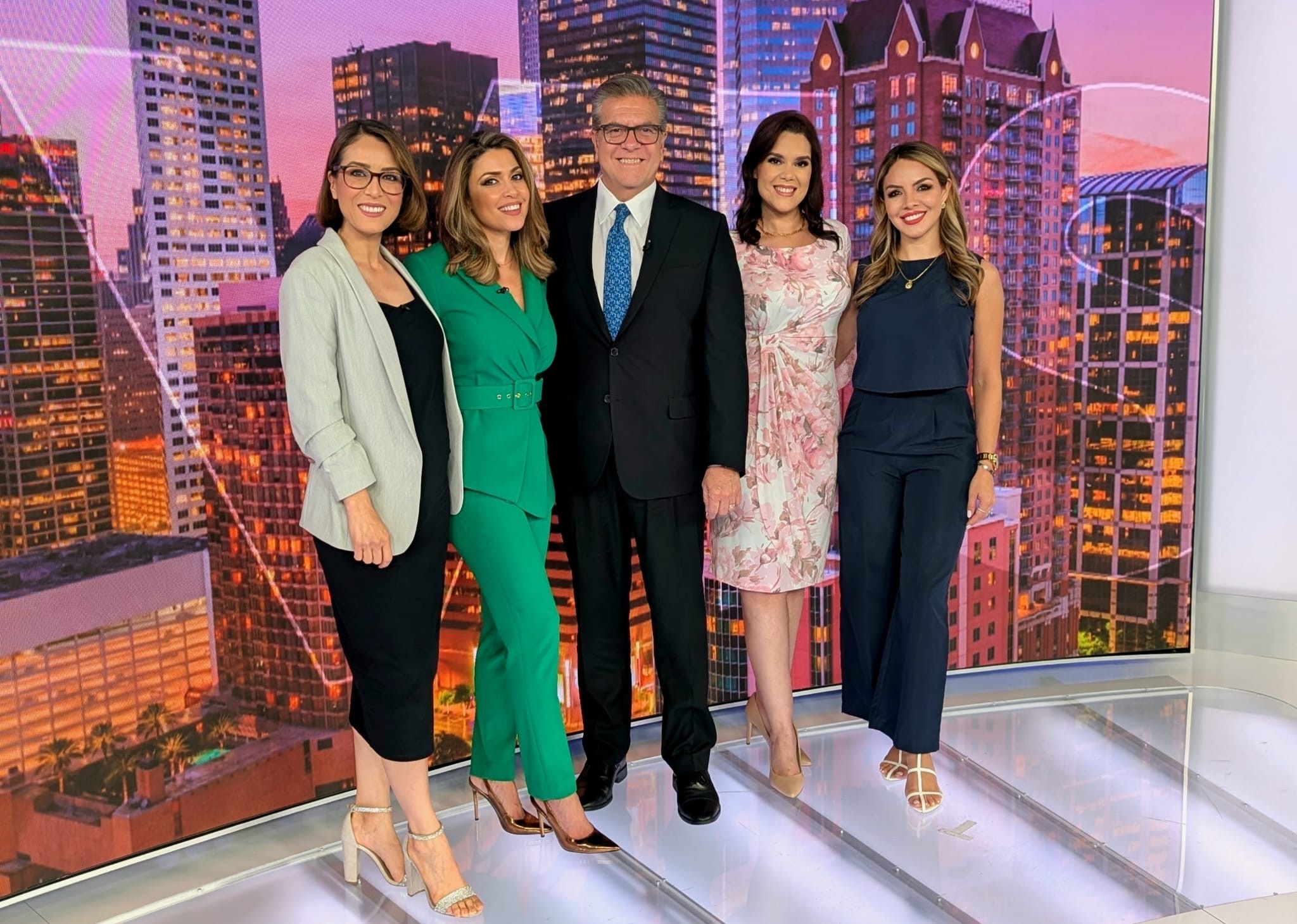 Five people standing together in front of a cityscape backdrop, smiling, dressed in formal and semi-formal attire.
