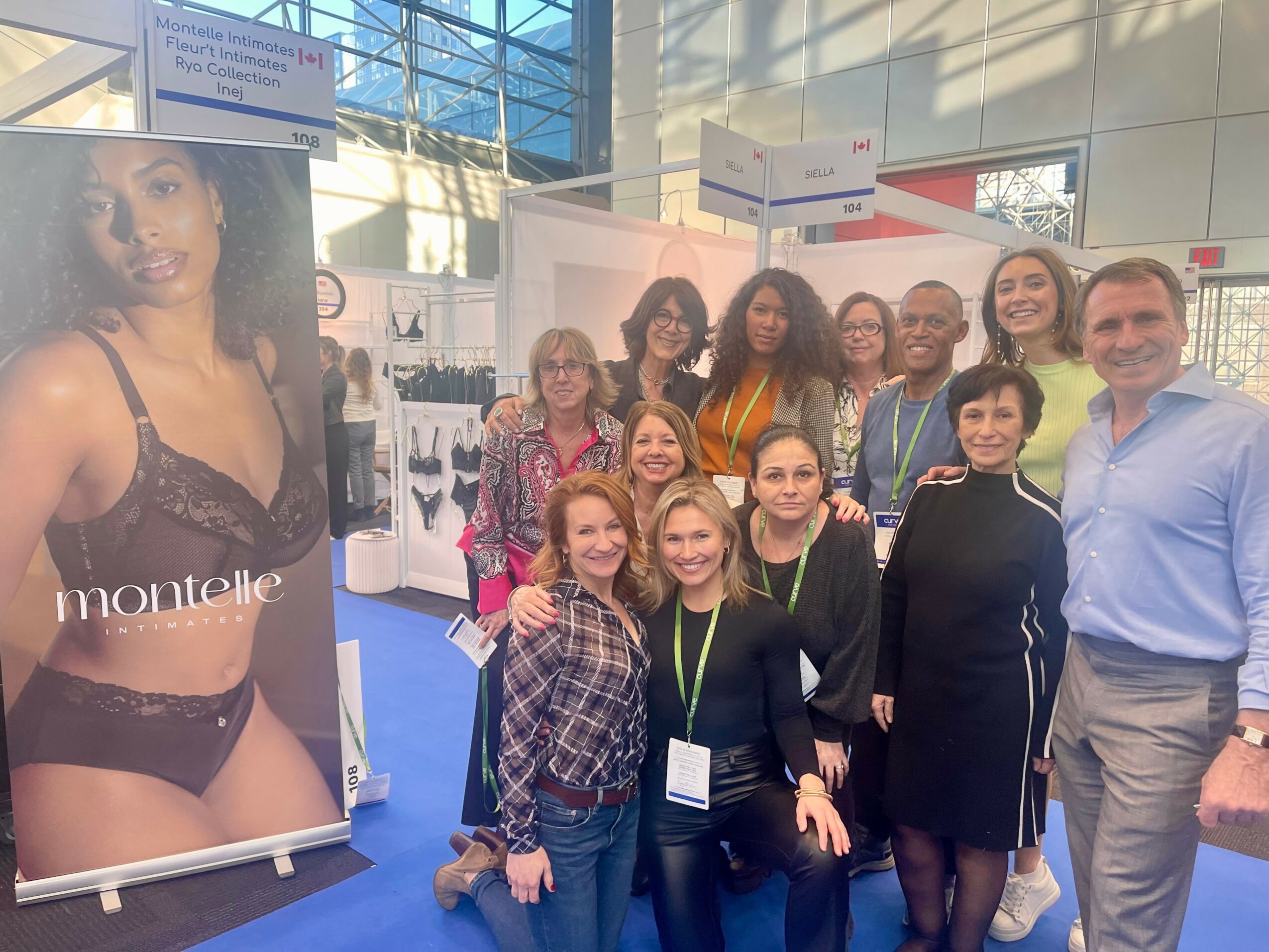 Group of people posing at an indoor event, with a large poster of a woman in lingerie on the left side.