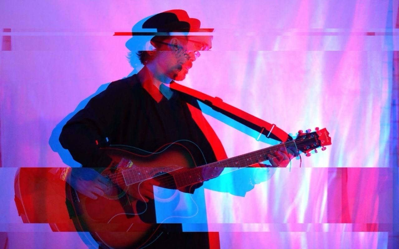 Person playing guitar with colorful, distorted visual effects and glitch-like appearance.