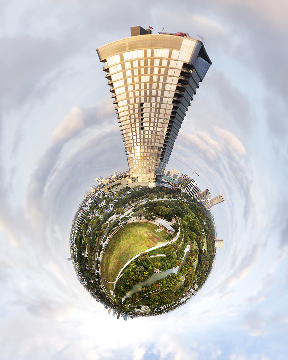 A distorted panoramic view of a cityscape with a tall building, green park, and cloudy sky, in a tiny planet style.