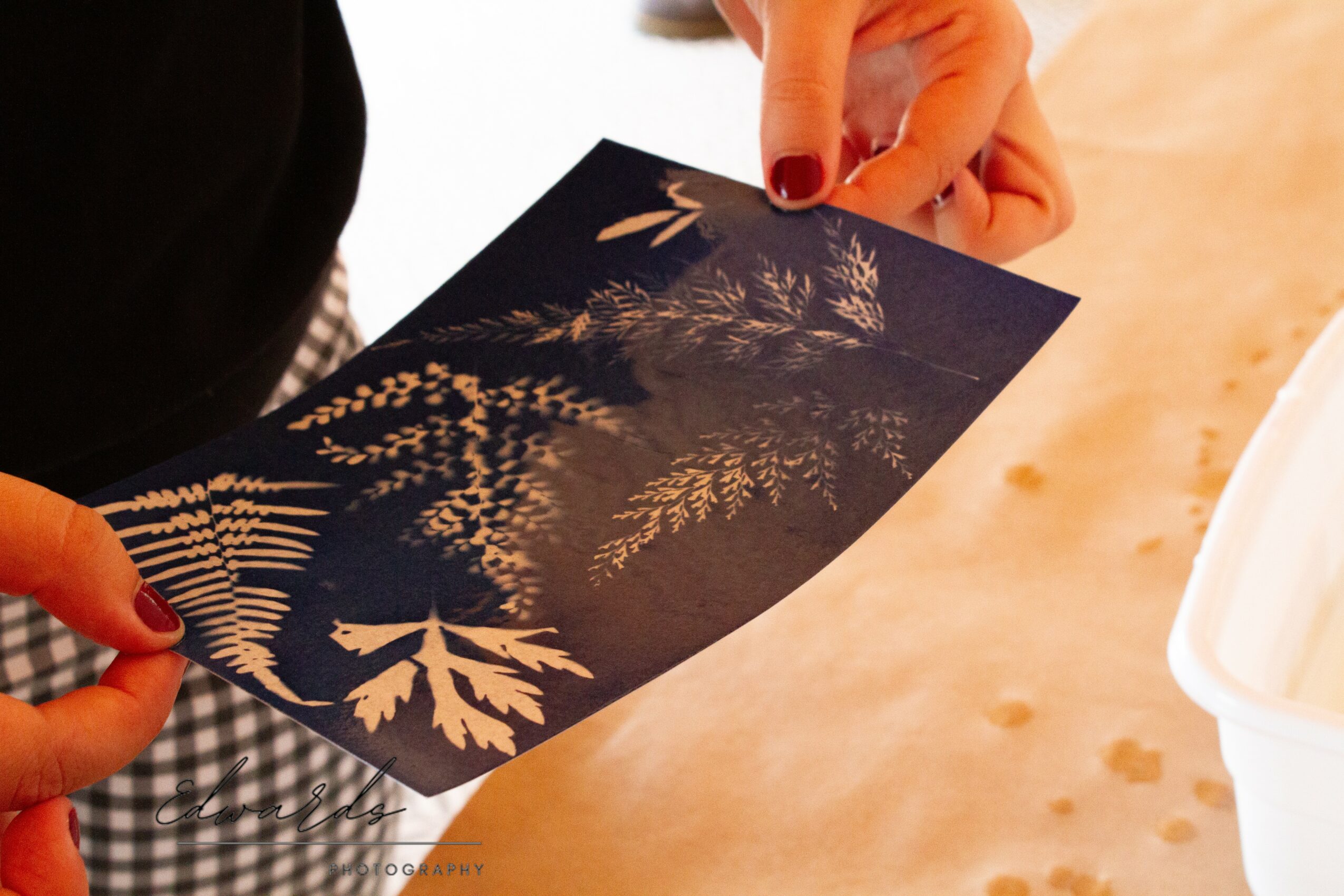 Person holding a dark-colored card with gold leaf and plant designs, resting on a light wooden surface.