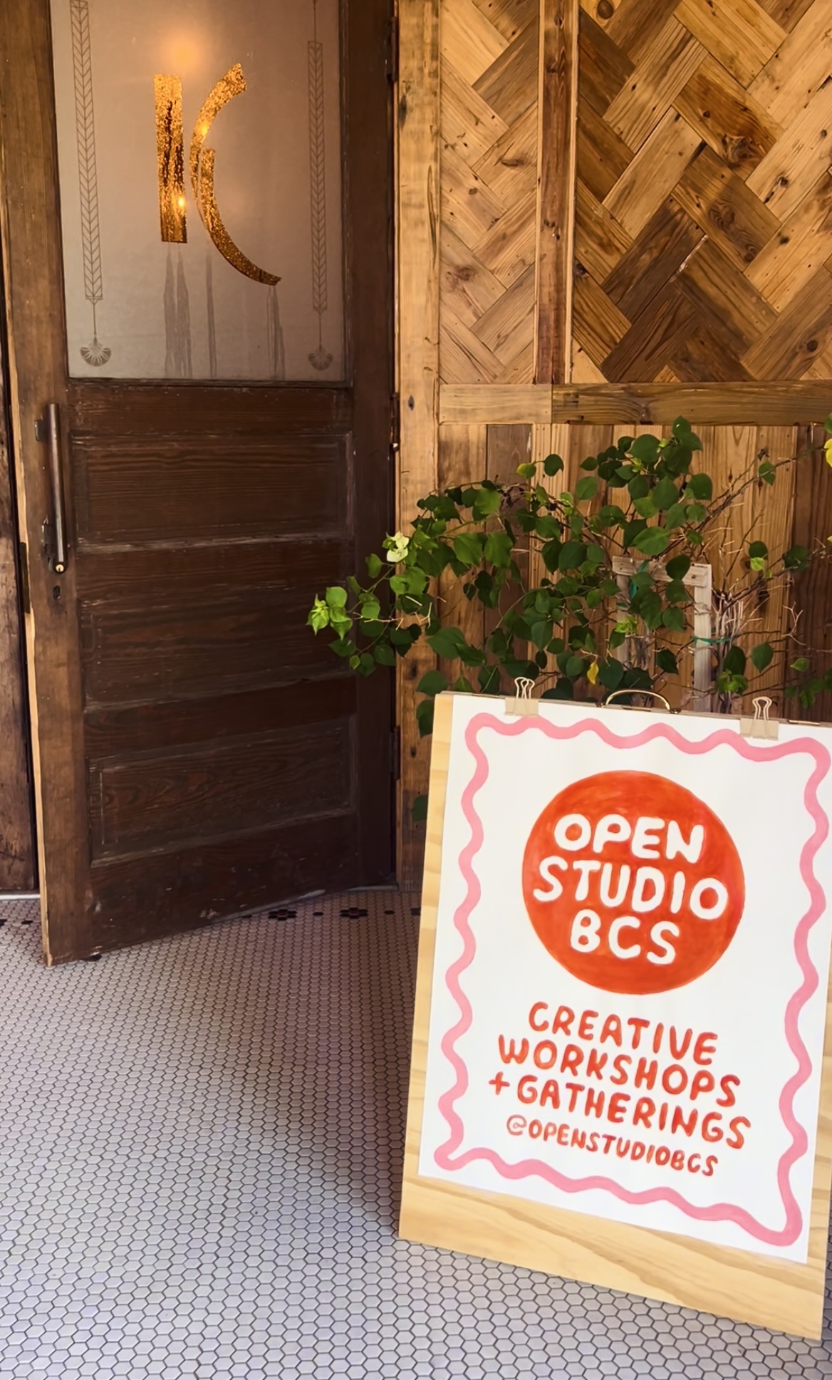 Door with a sign advertising open studio workshops, creative gatherings, and workshops, with a plant nearby.
