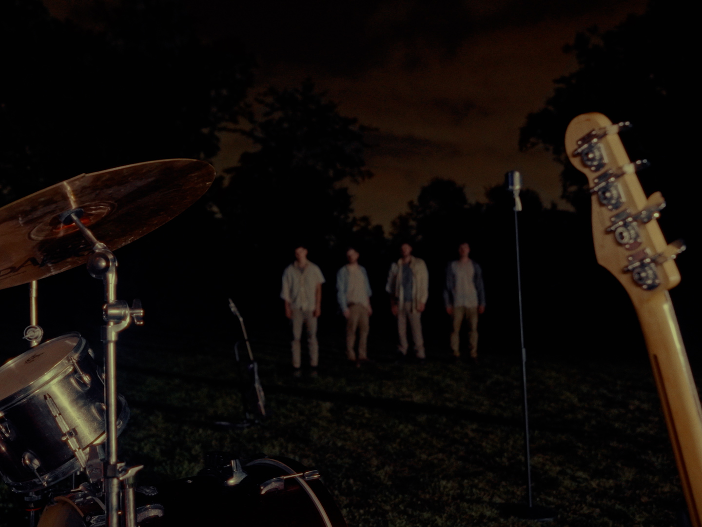 Four people standing outdoors at night, with musical instruments and equipment visible in the foreground.