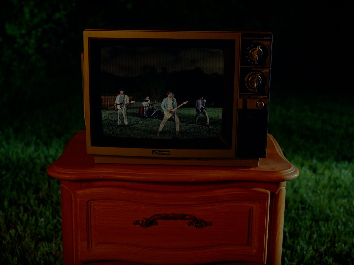 A vintage television on a wooden stand displays a scene with people and animals outdoors at night.