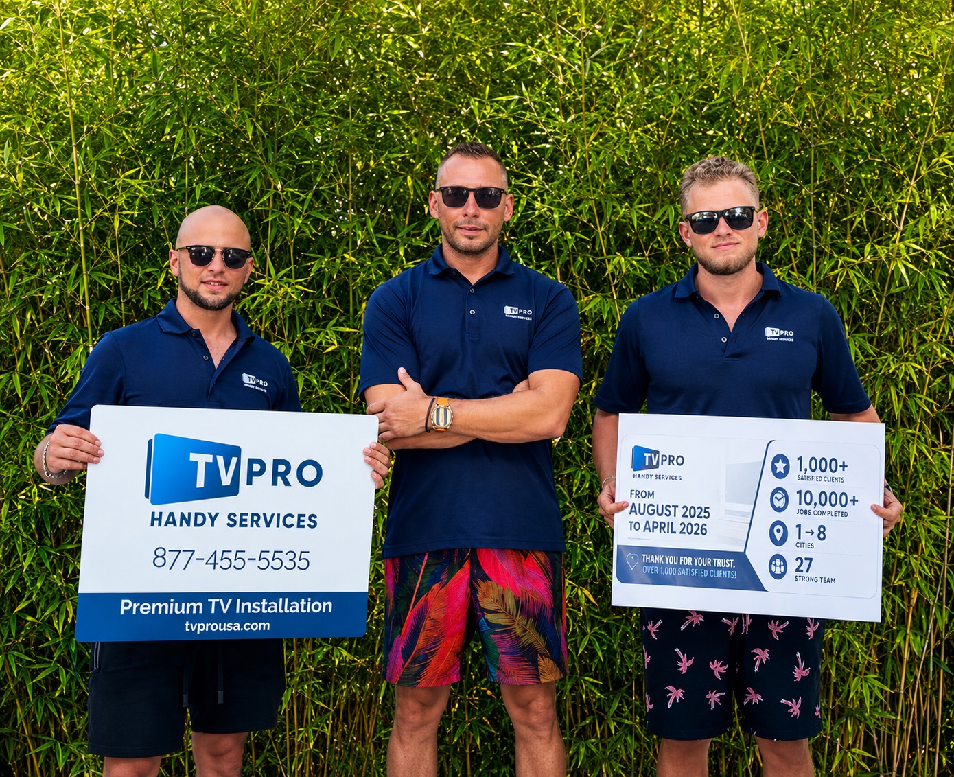 Three men in dark shirts and sunglasses standing outdoors in front of green foliage, holding signs with company information.