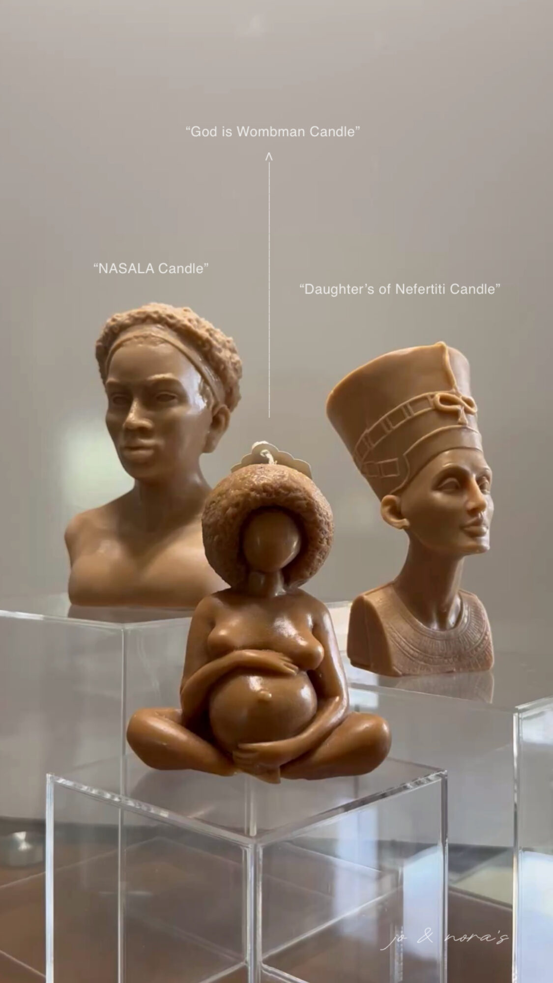Three sculptures of African women and a child, with the child holding a doughnut, displayed on clear pedestals.