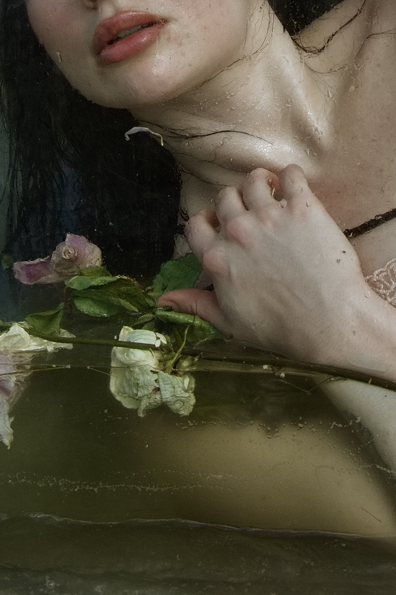 Close-up of a person's face, hand, and part of their chest with water and a pink flower nearby.