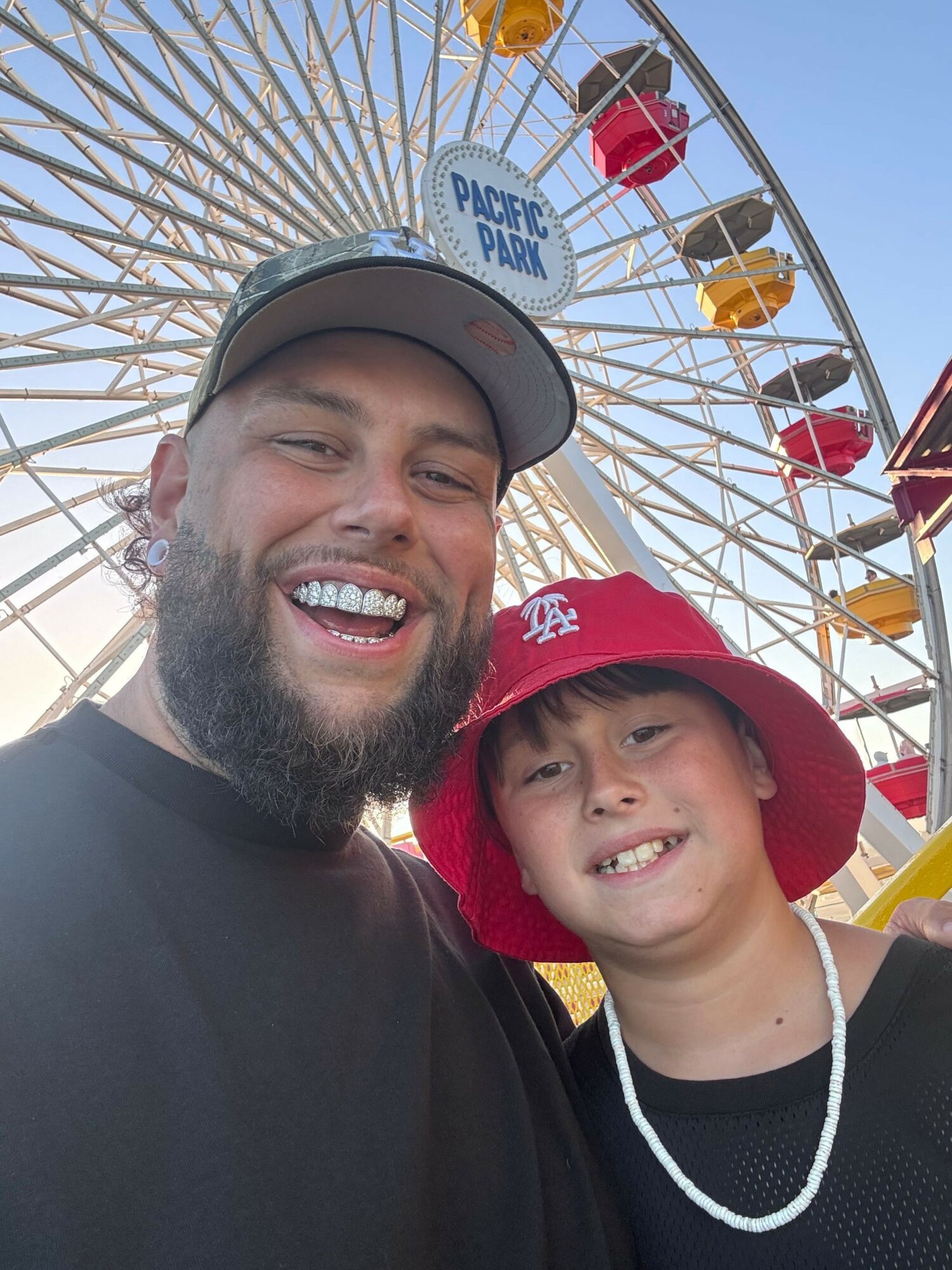 Two smiling people taking a selfie in front of a Ferris wheel at an amusement park.