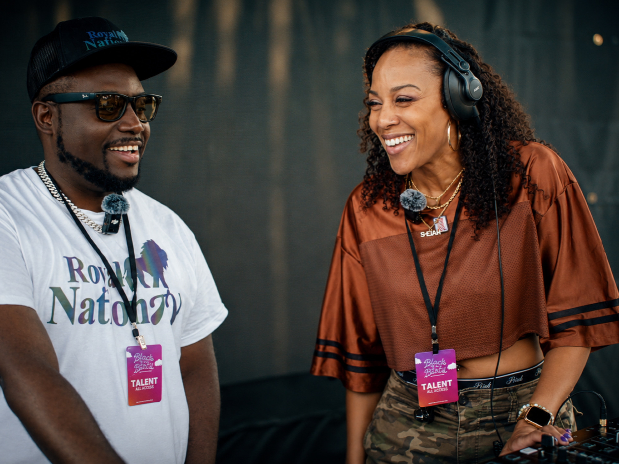 Two people smiling and talking, one wearing headphones, in a professional setting, with a dark background.