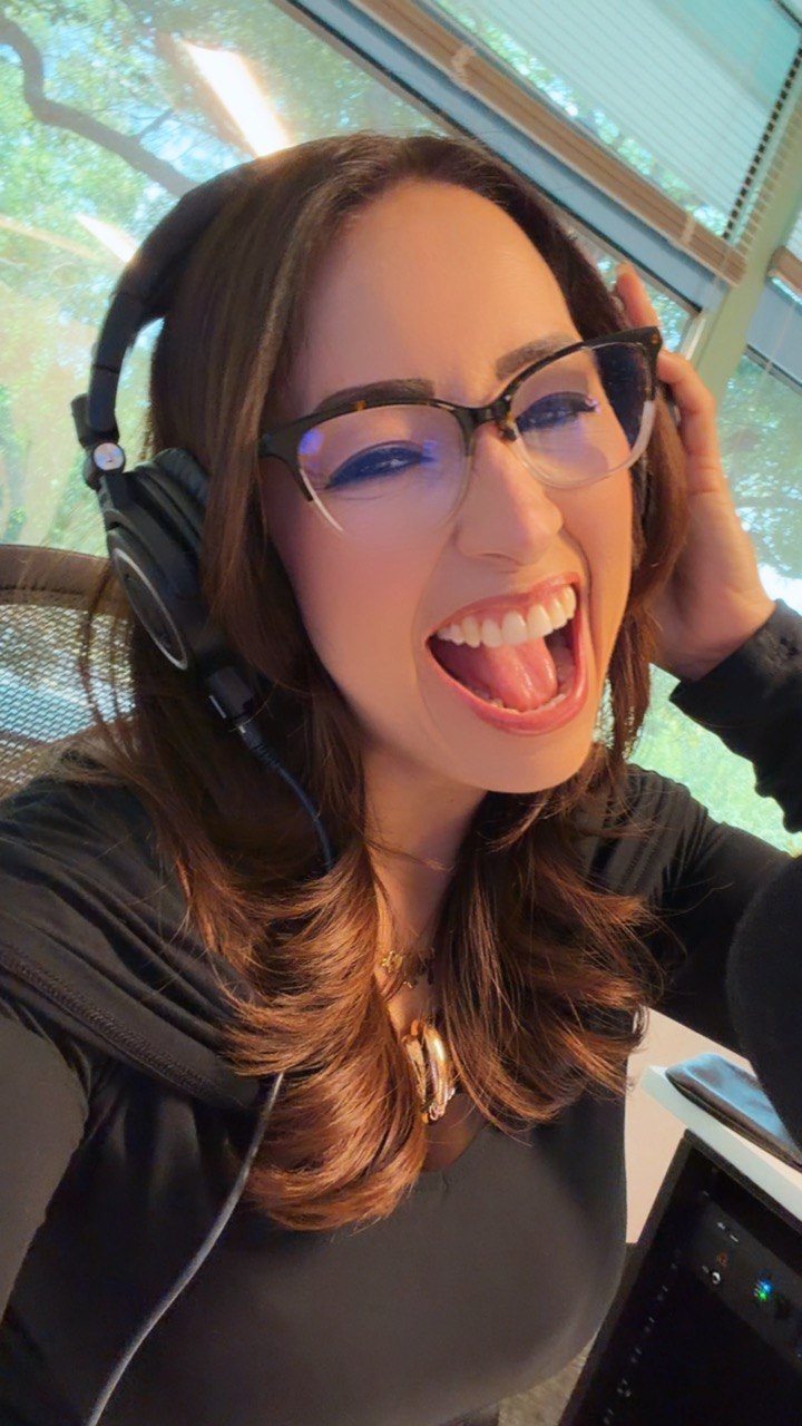 Woman with glasses and headphones smiling and sticking out tongue, indoors with window and trees outside