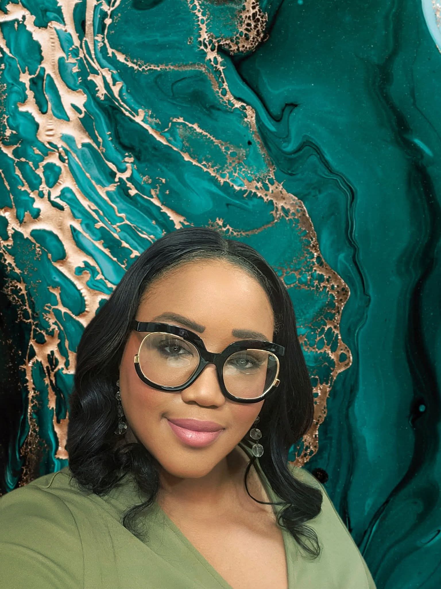 Woman with black hair, glasses, and makeup, standing in front of a teal and gold abstract background.