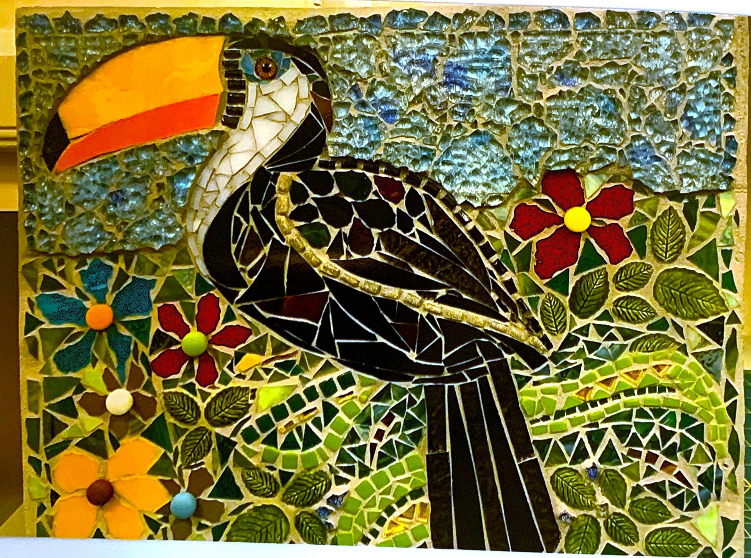 Colorful mosaic of a toucan bird with a large orange beak, surrounded by flowers and green foliage.