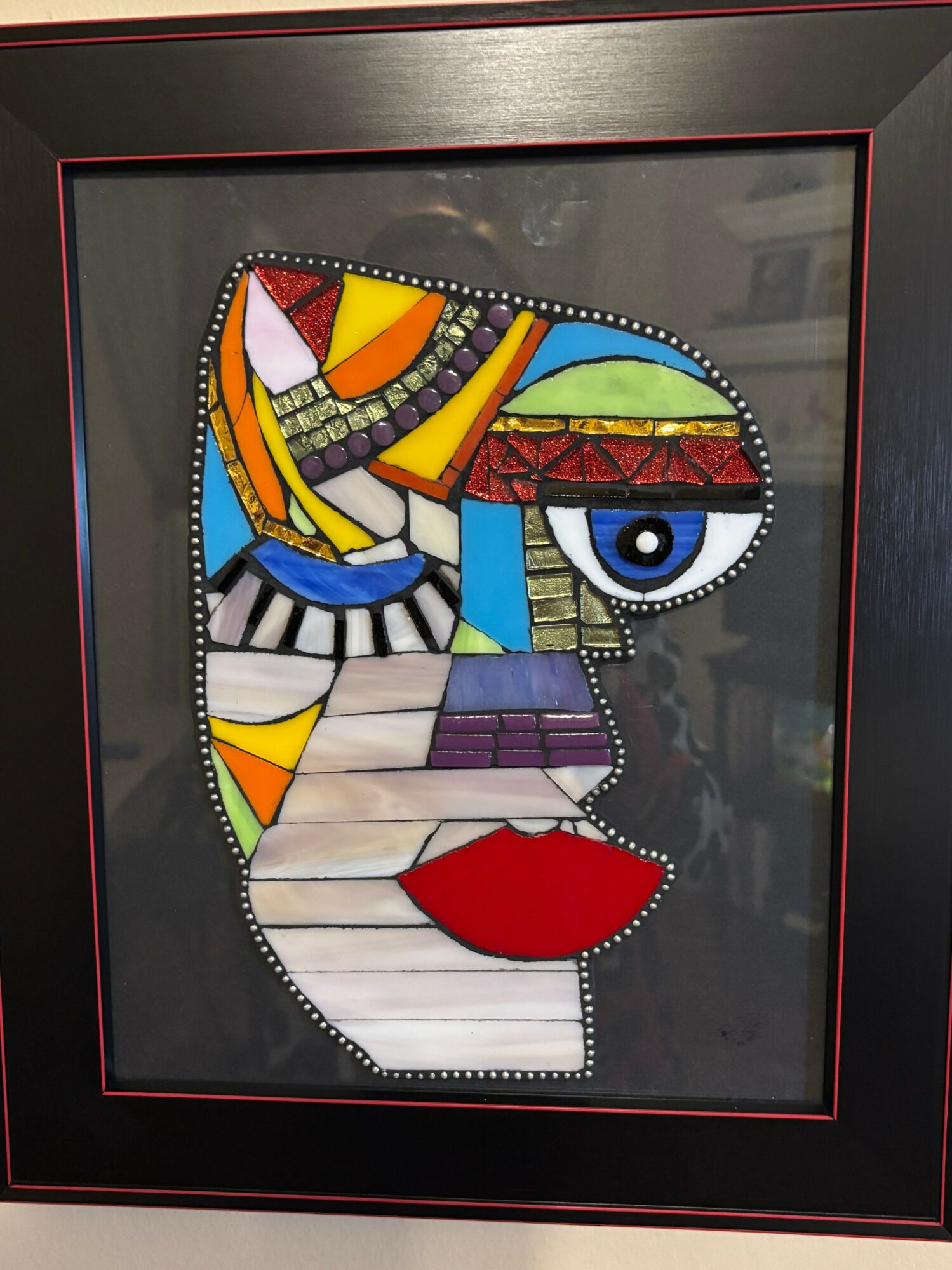 Abstract mosaic portrait of a face with colorful geometric shapes, including an eye and red lips, on a black background.