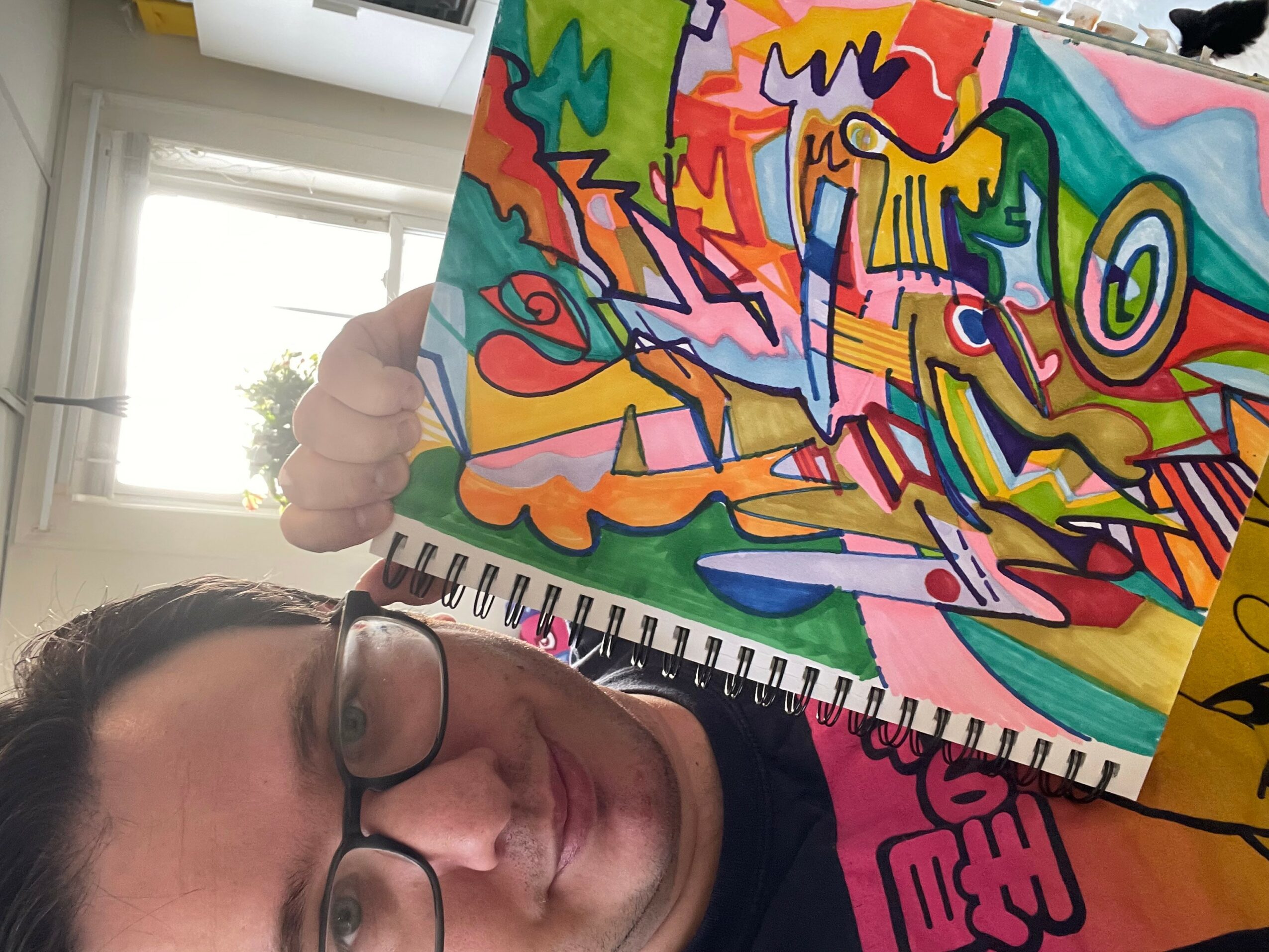 Person holding colorful abstract artwork in a room with window and natural light.
