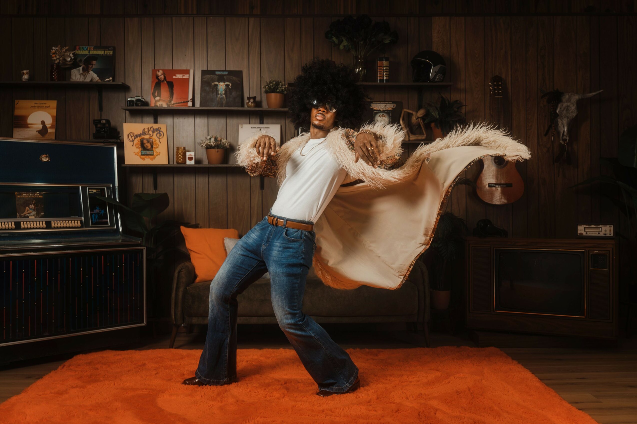 Person dancing in a room with wooden walls, shelves, and a red carpet, wearing a white top and flared jeans.