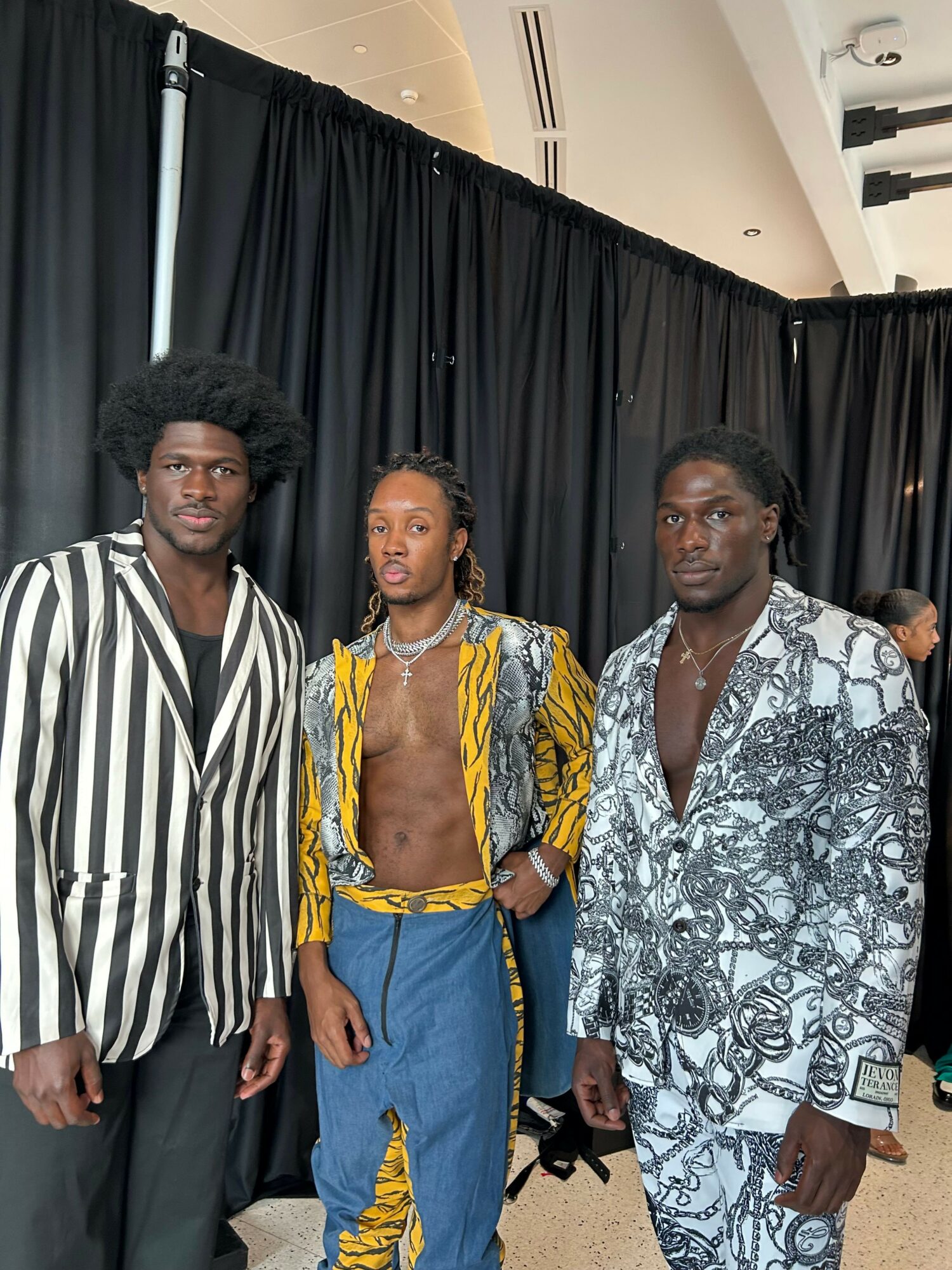 Three people standing together in front of a black curtain, wearing colorful and patterned clothing, posing for a photo.