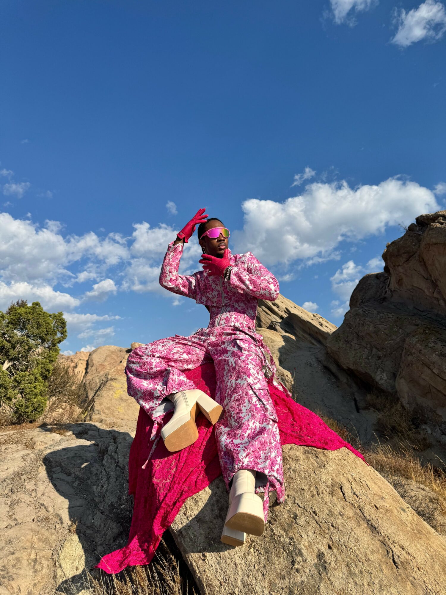 Person in pink and purple climbing gear on rock face, blue sky with clouds in background.