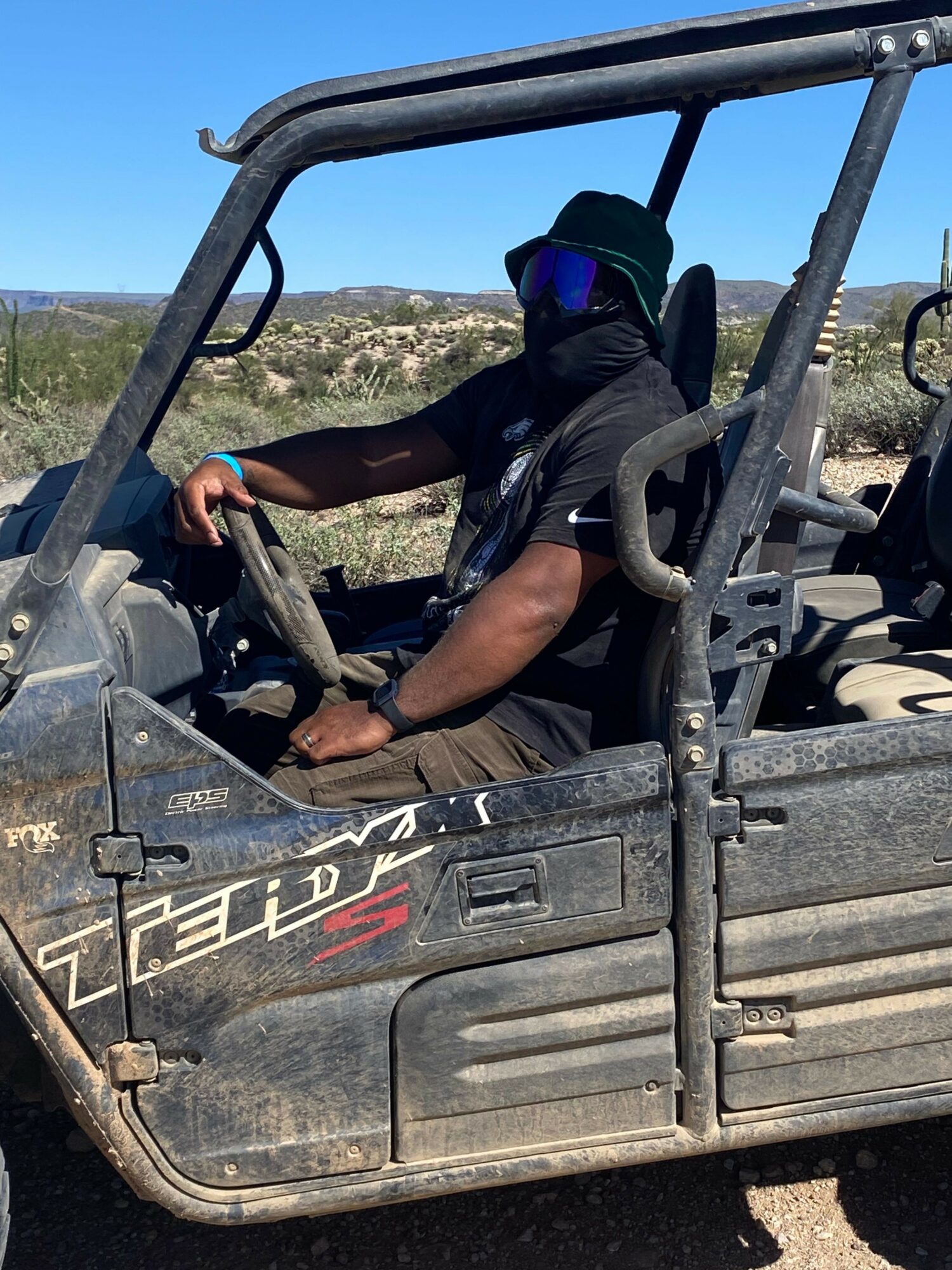 Person wearing a helmet and backpack sitting in a utility vehicle, holding a tool, with a landscape background.