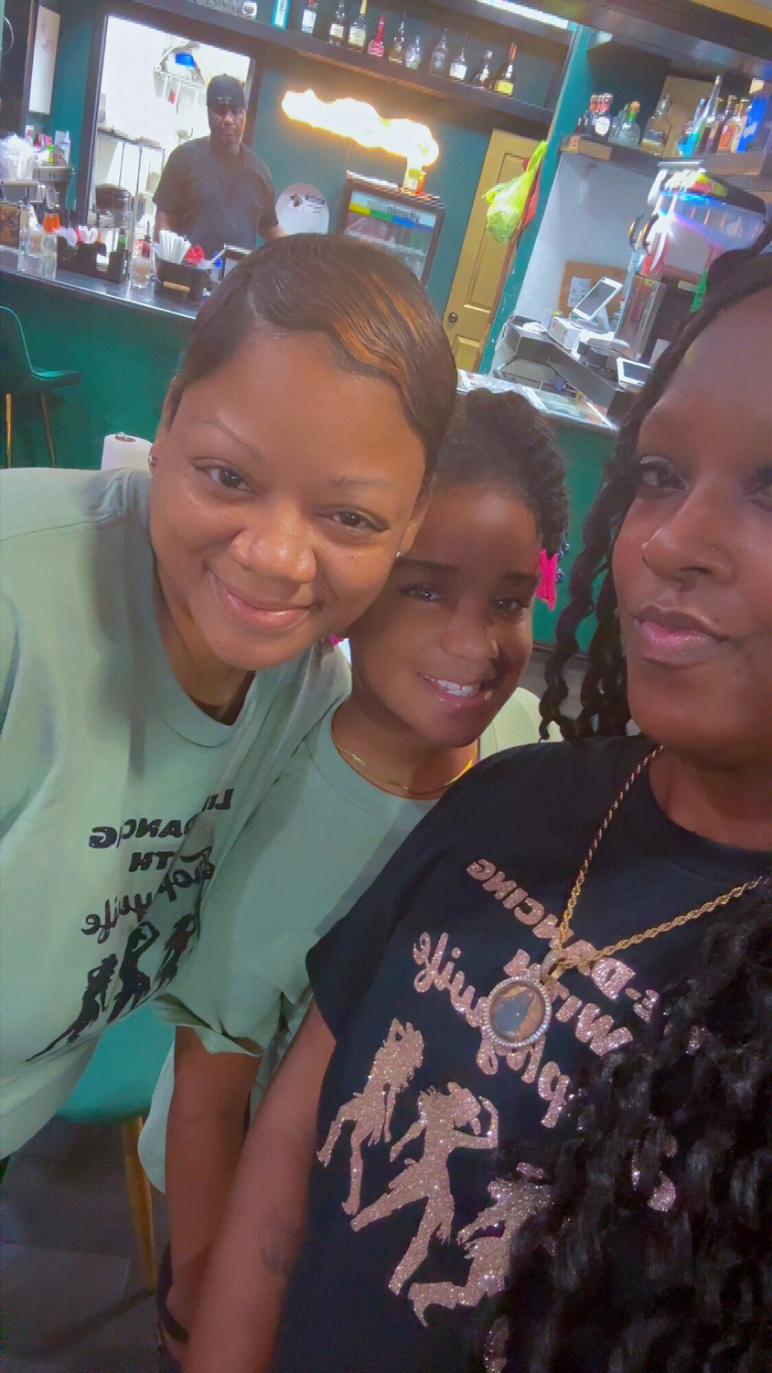 Three people smiling in a bar or restaurant setting with a bartender in the background.