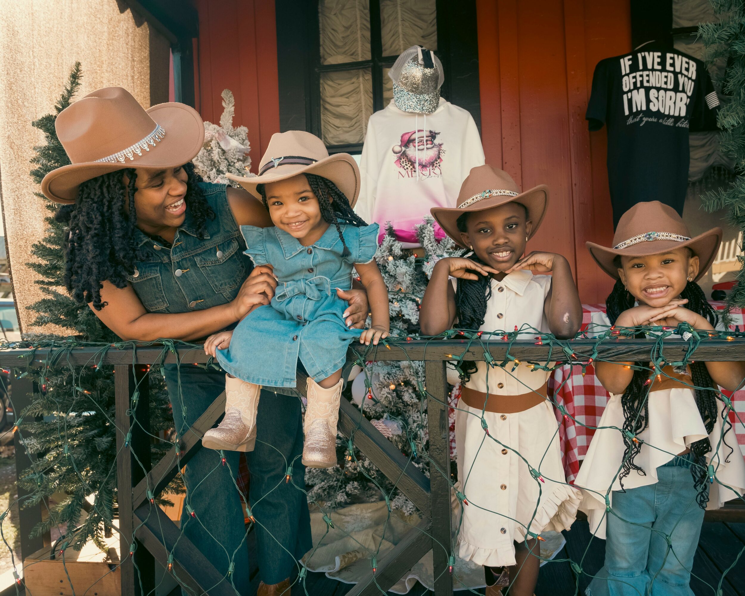 Four children wearing cowboy hats and casual clothes stand behind a black railing, smiling outdoors.