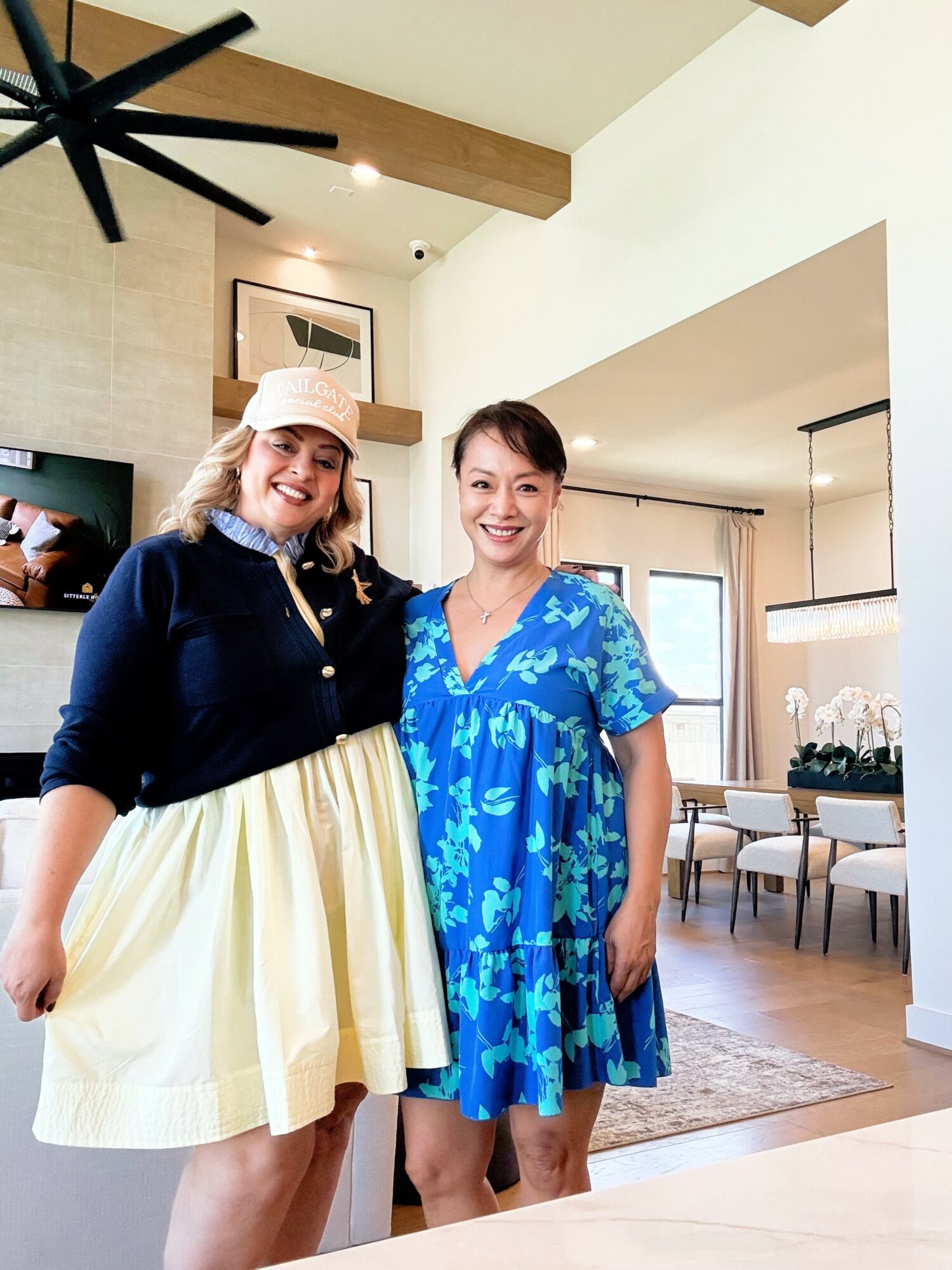 Two women standing in a bright, modern living room, smiling, with a dining area in the background.