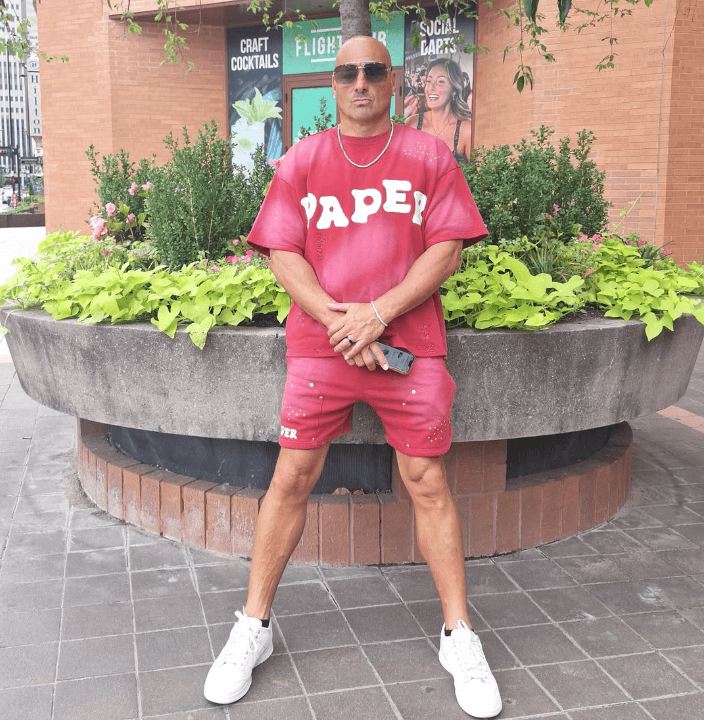 Man in red outfit with sunglasses standing in front of a large flower planter outdoors.