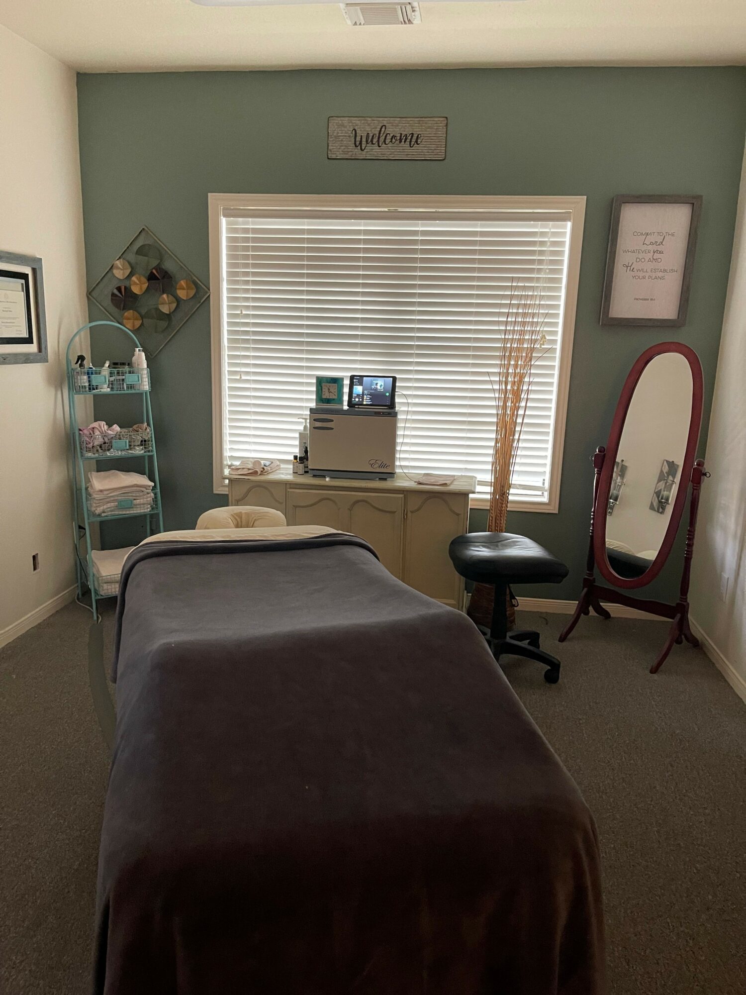 Room with a window, mirror, and massage table, with a small sign on the wall, and various items near the window.