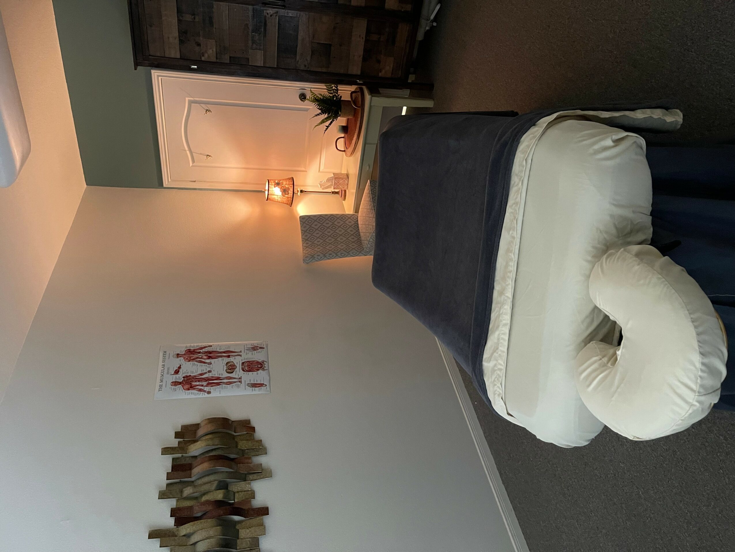 A massage table with a face cradle in a room with a door, lamp, and wall art.