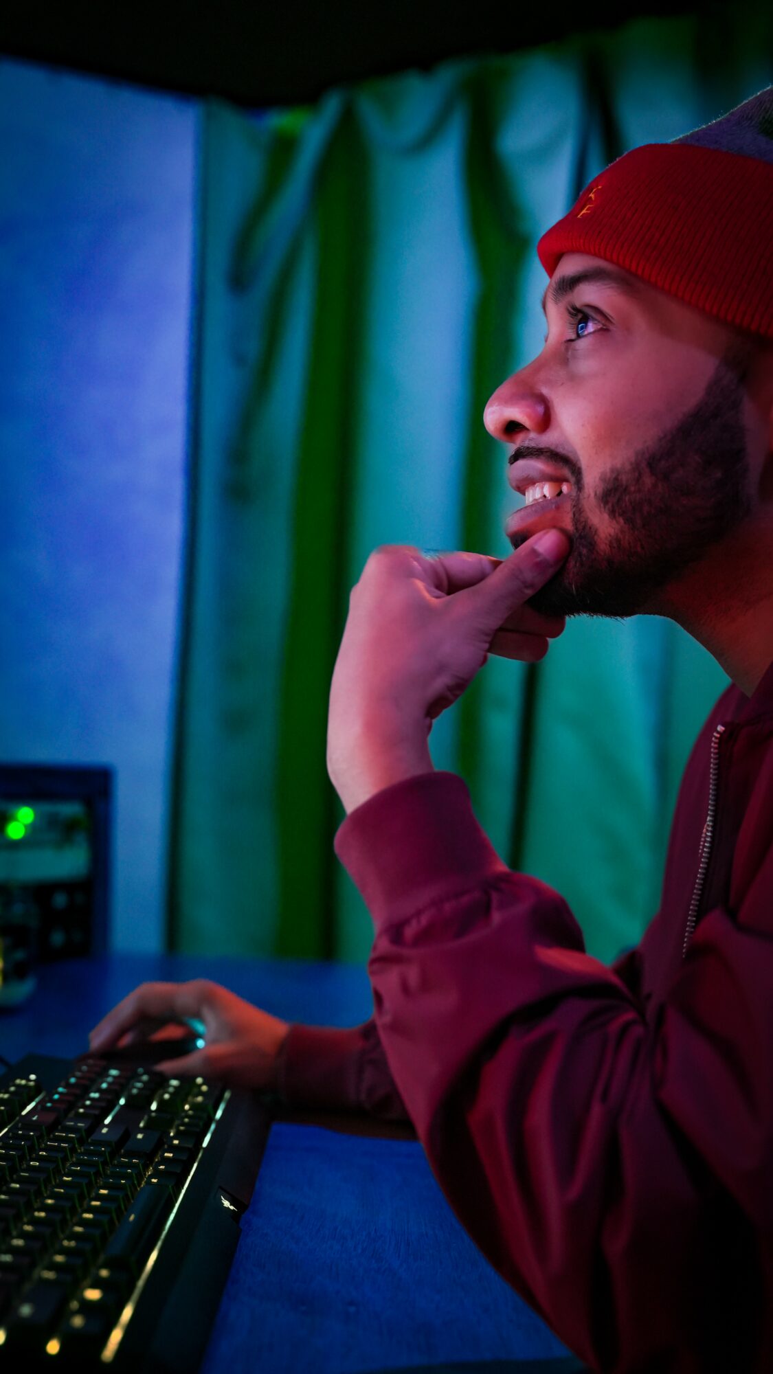 Side profile of a man wearing a red head covering, looking at a computer screen with a thoughtful expression.