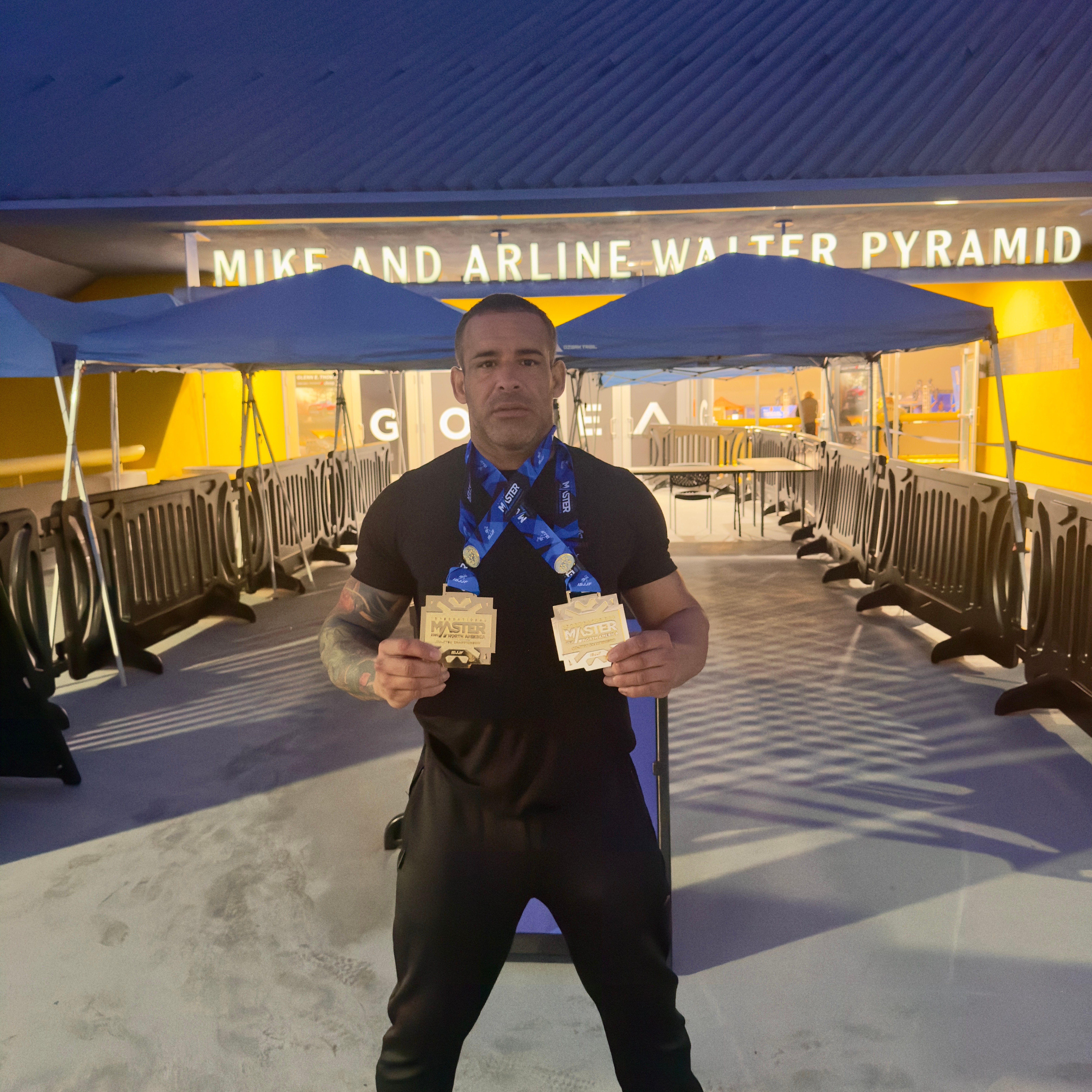 Man holding two medals in front of a yellow and blue background with a sign reading 'Mike and Airline Walter Pyramid'.