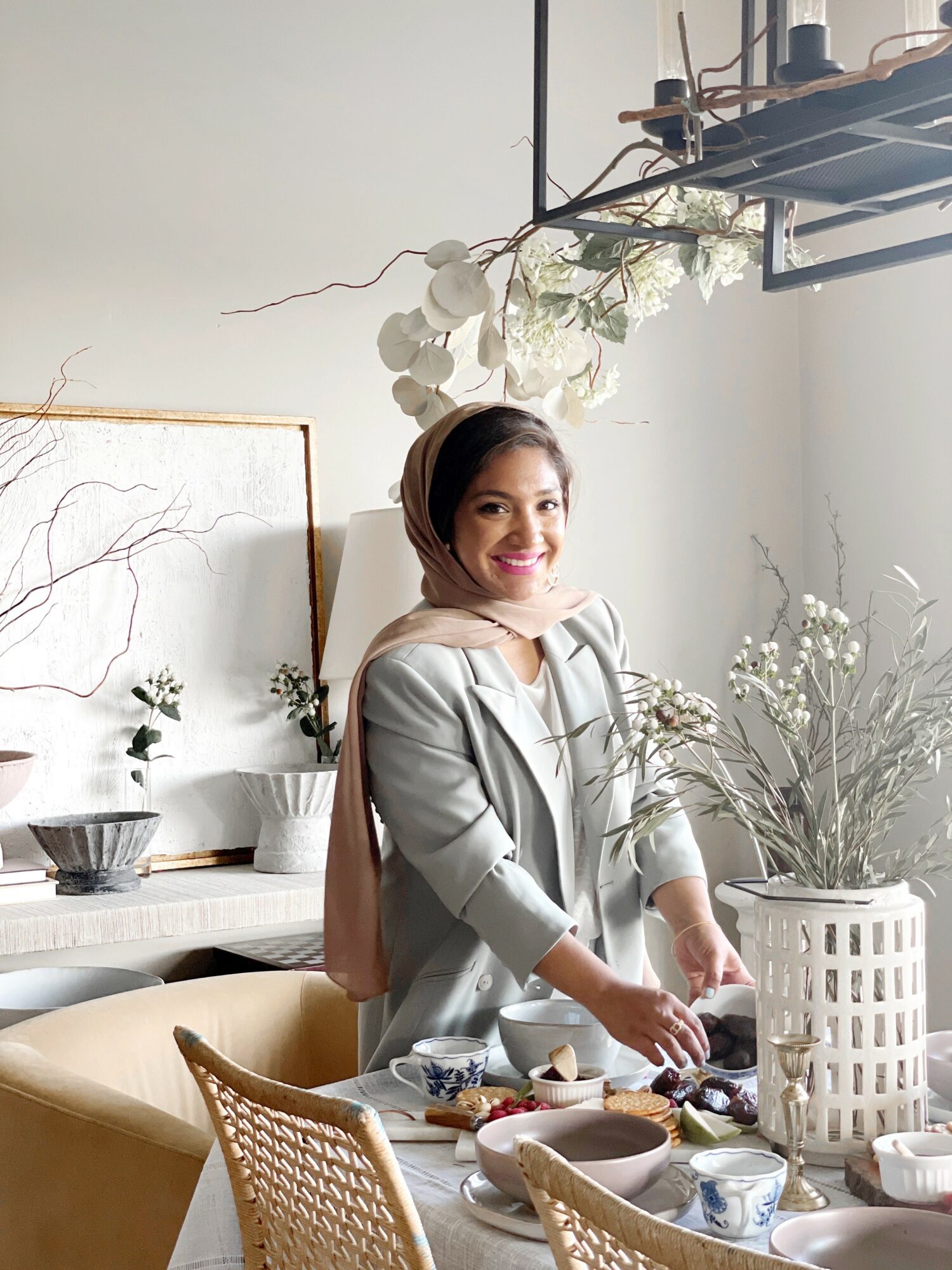 Woman smiling at a table with dishes and decorative plants in a bright room.